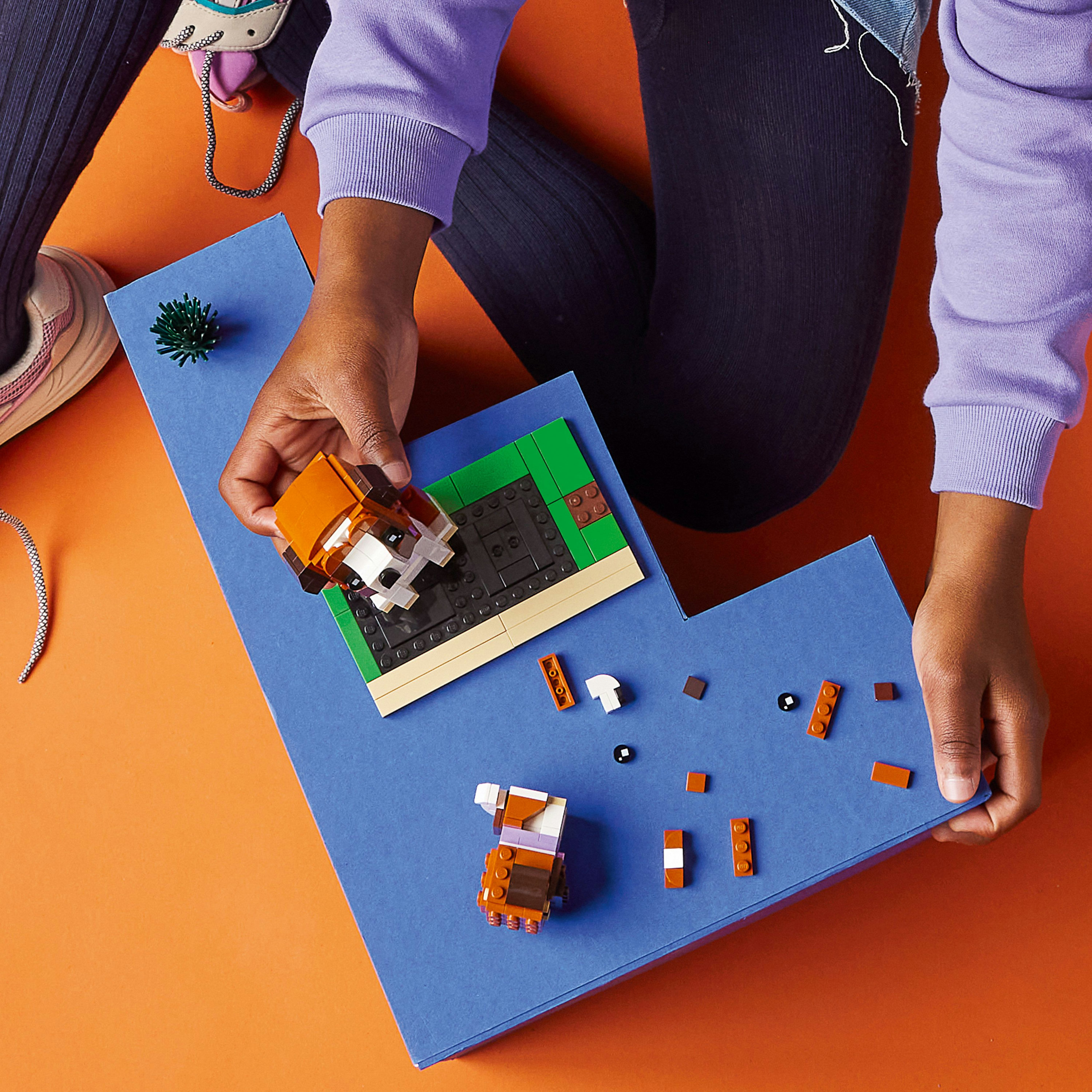 Ein Kind baut einen Lego-Hund auf einer blauen Oberfläche zusammen, weitere Legosteine liegen daneben. Orange Hintergrund.
