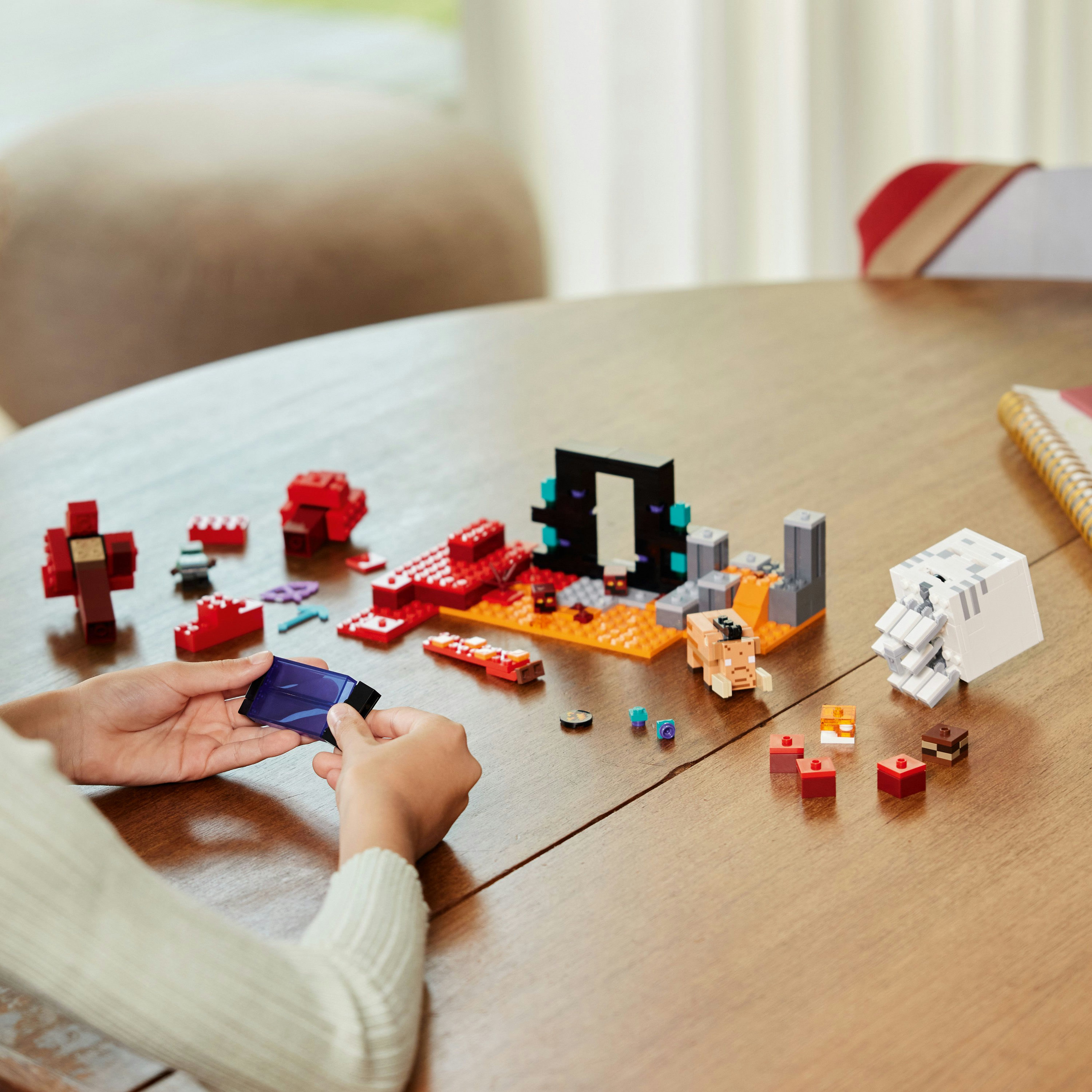 Hands assemble a Lego Minecraft set, with a portal and figures on a wooden table.