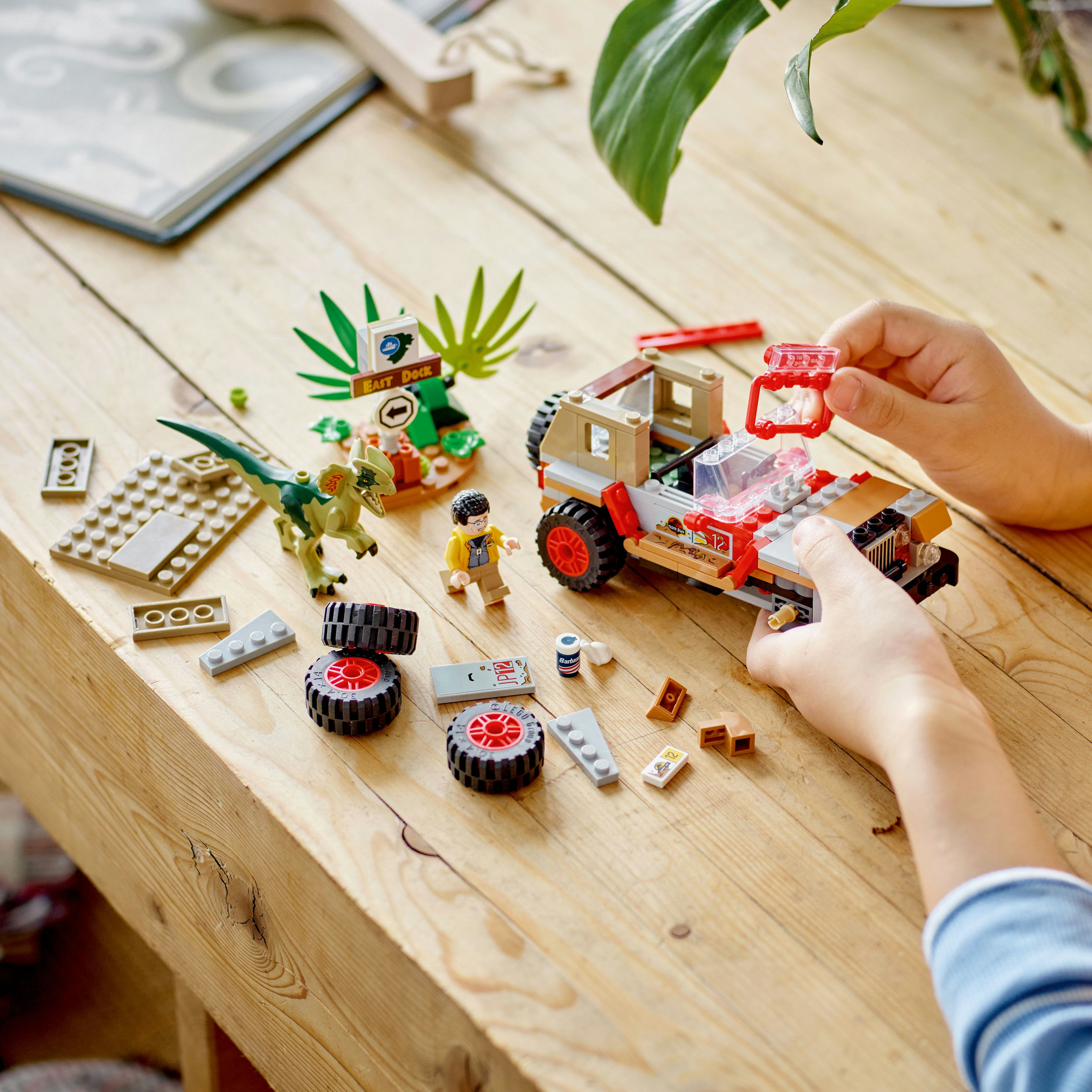 Ein Kind spielt mit einem Lego-Set zum Thema Dinosaurier auf einem Holztisch, einschließlich eines Jeeps, eines Dinosauriers und Legosteinen.