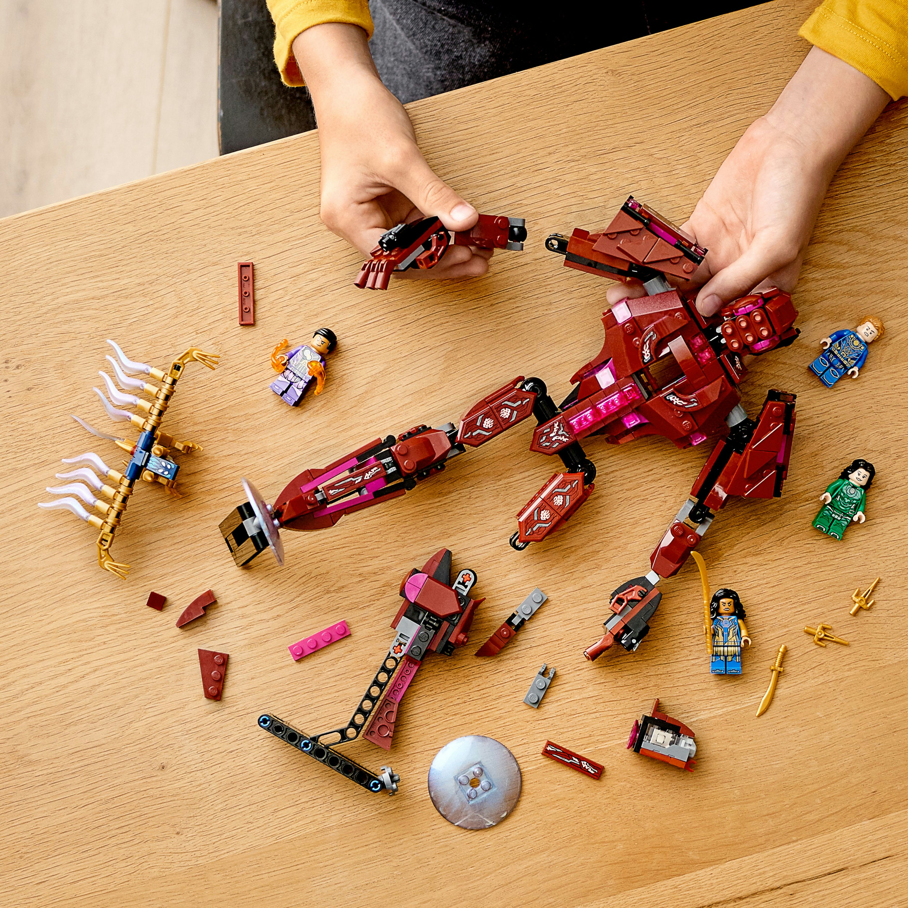 Hände, die eine Lego-Figur konstruieren, mit verstreuten Teilen. Braune und violette Komponenten sind sichtbar.