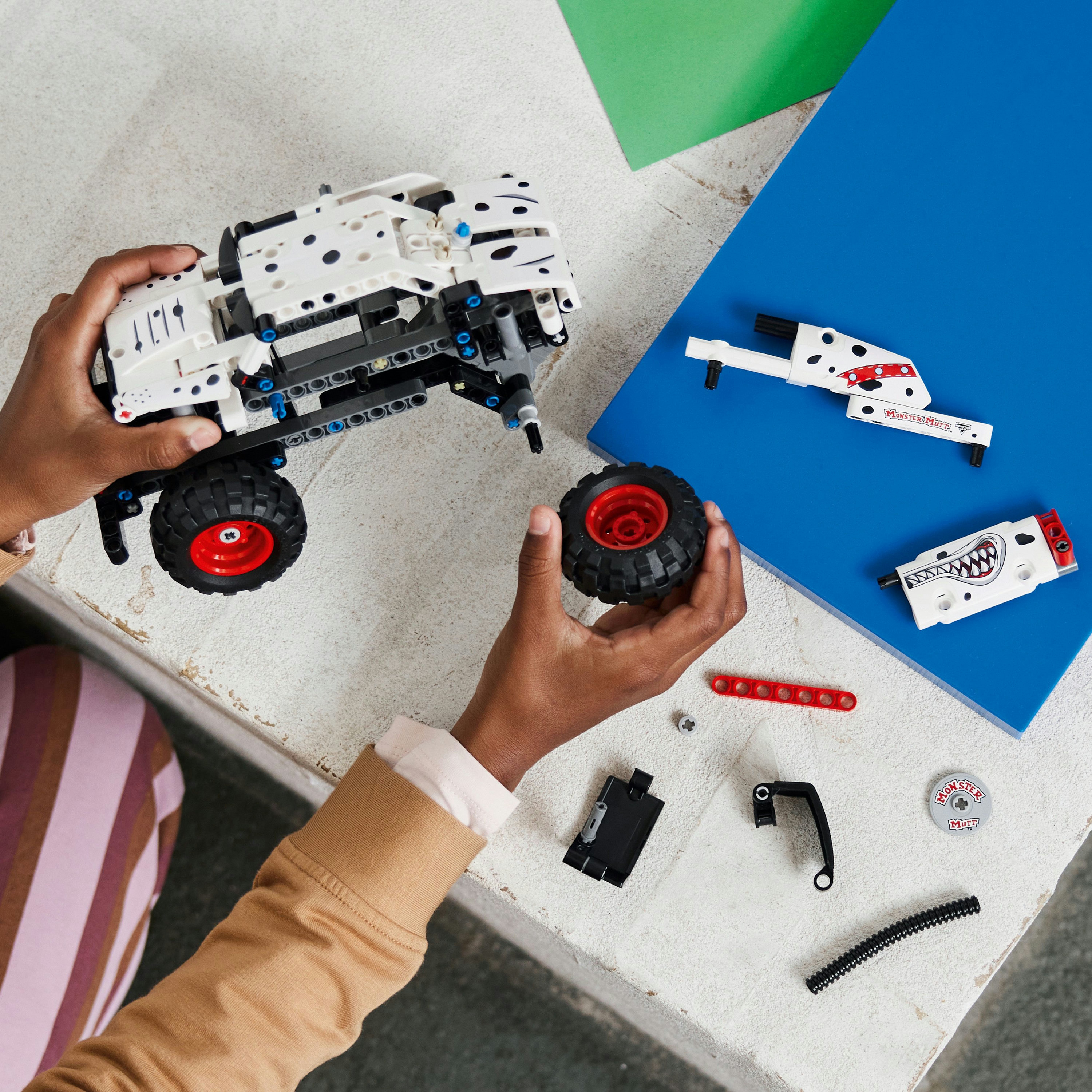 Hände, die einen weißen und schwarzen Lego Monstertruck mit roten Felgen zusammenbauen.