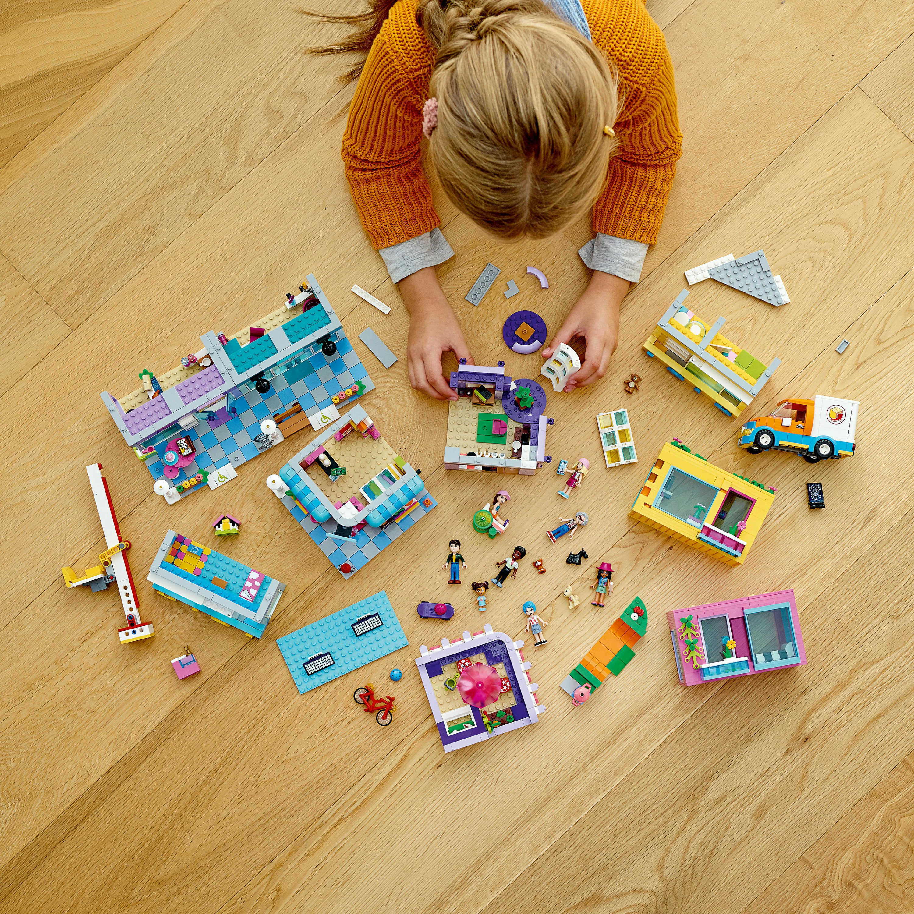 Een kind dat met Lego-stukken speelt. Lego huizen en figuren zijn op de vloer gerangschikt.