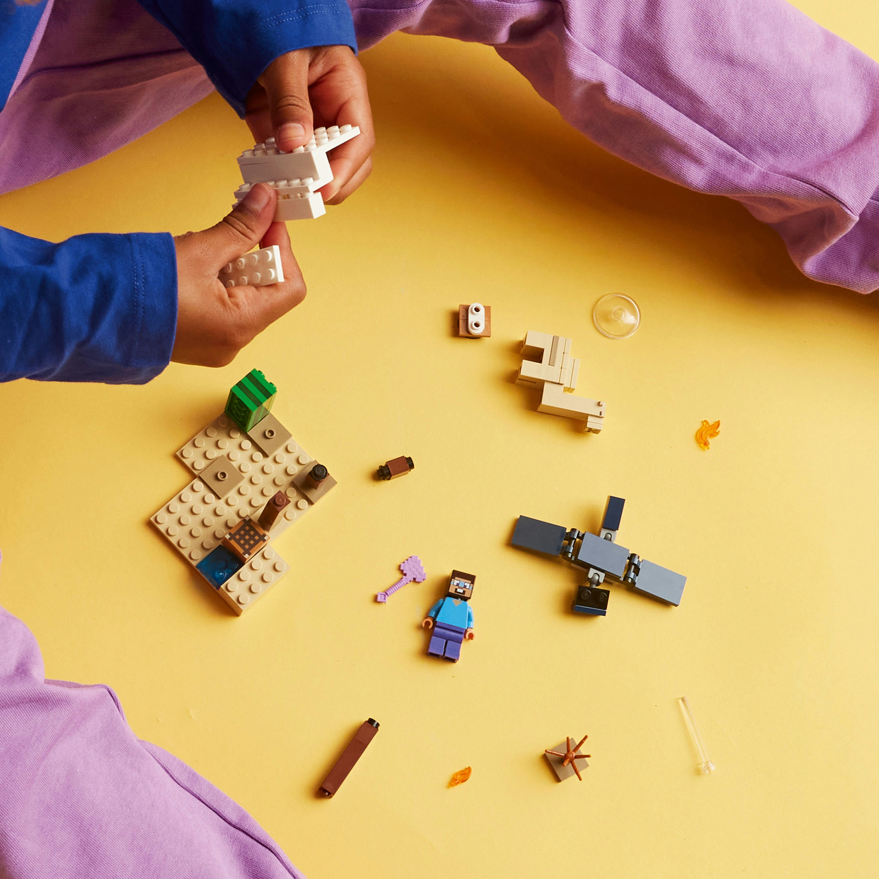 Mains assemblant des briques Lego sur une surface jaune. Diverses pièces Lego et une figurine Minecraft sont éparpillées.