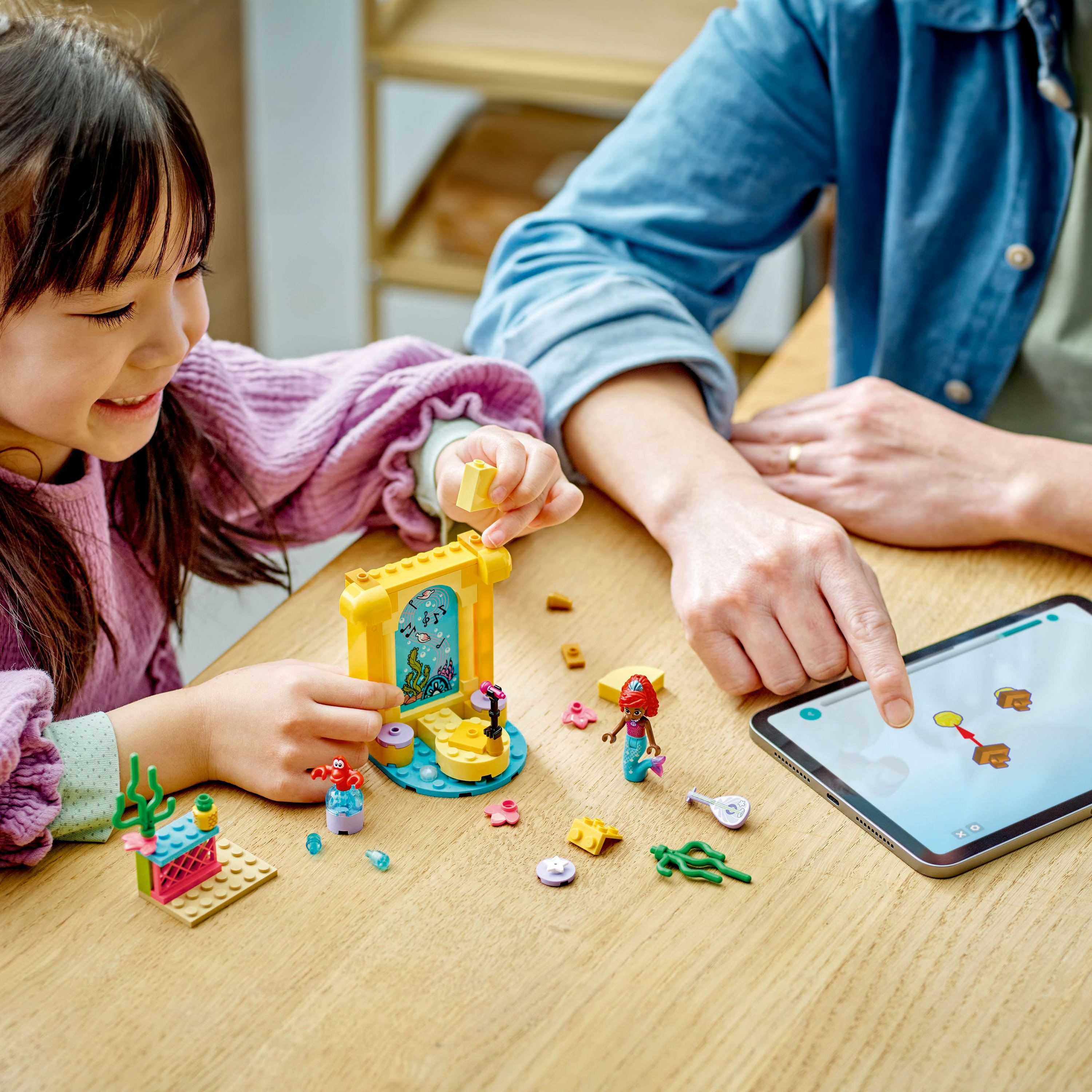 Dziecko i dorosły wchodzą w interakcję z zestawem Lego Friends, na drewnianym stole z klockami Lego.