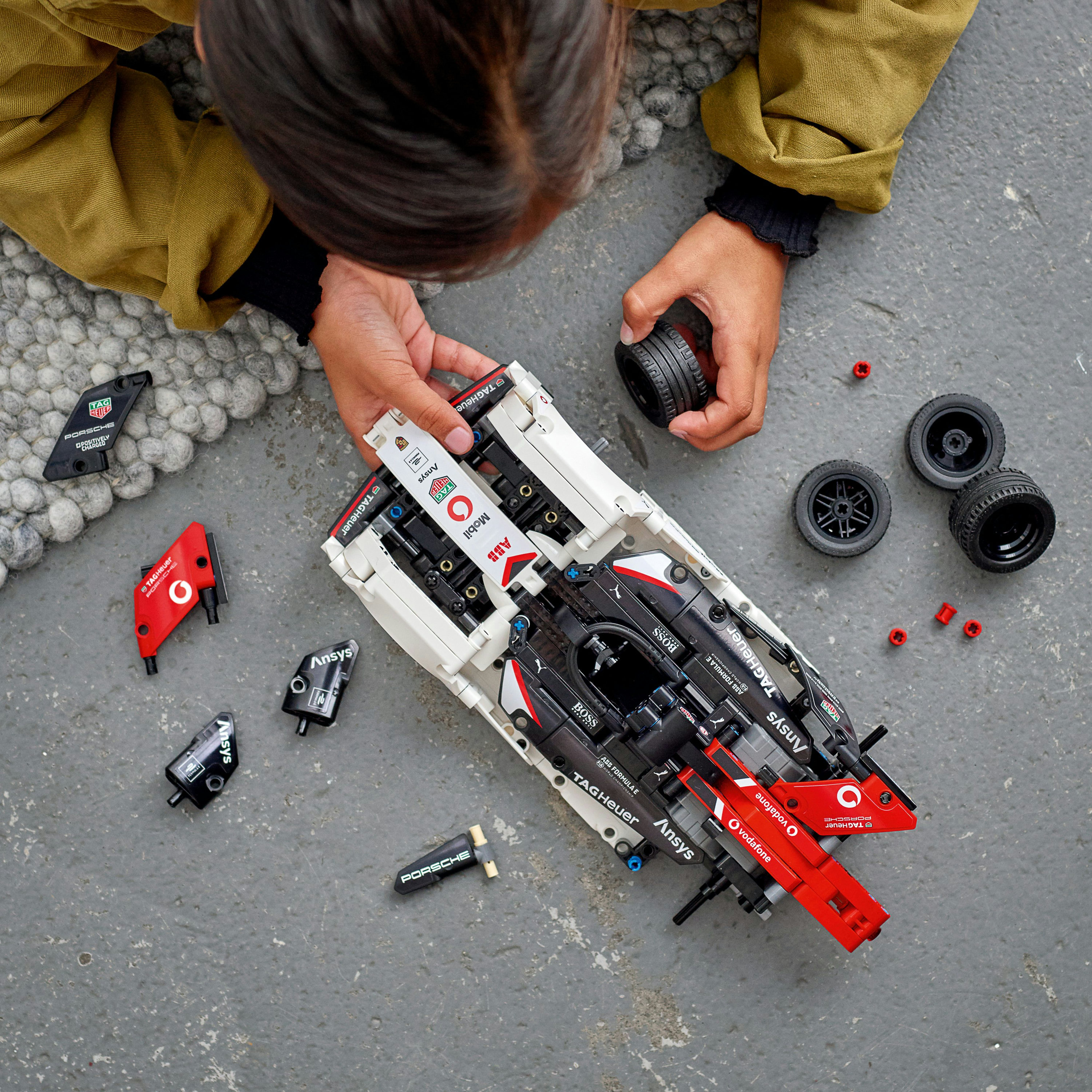 Kind spielt mit Lego Technic Rennwagen Teilen. Weißes und schwarzes Auto mit roten Details. Grauer Hintergrund.
