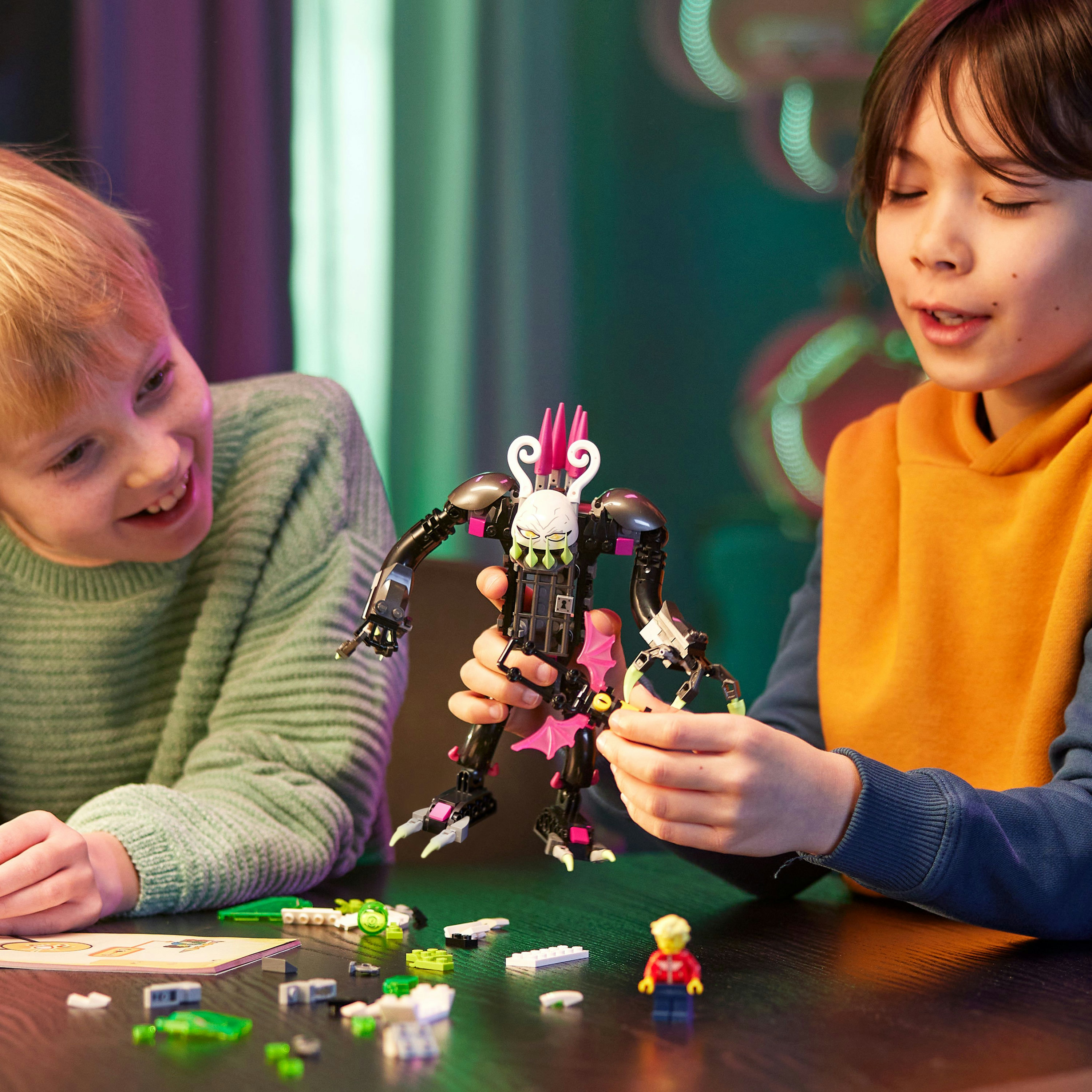 Zwei Kinder spielen mit einem LEGO Set. Enthält eine Monsterfigur und Zubehör auf schwarzer Oberfläche.