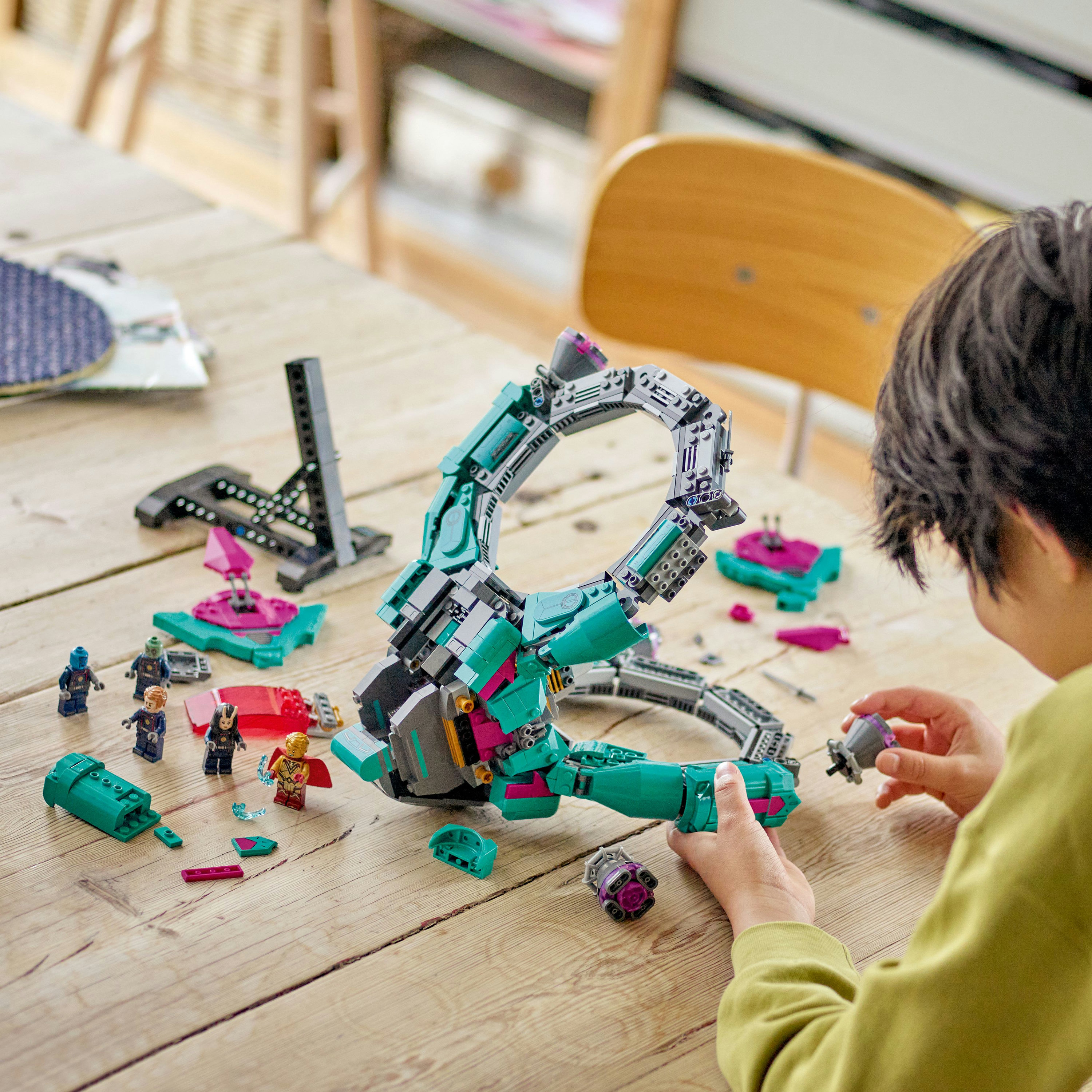 Dziecko składa kolorowy zestaw Lego na drewnianym stole, otoczone elementami.