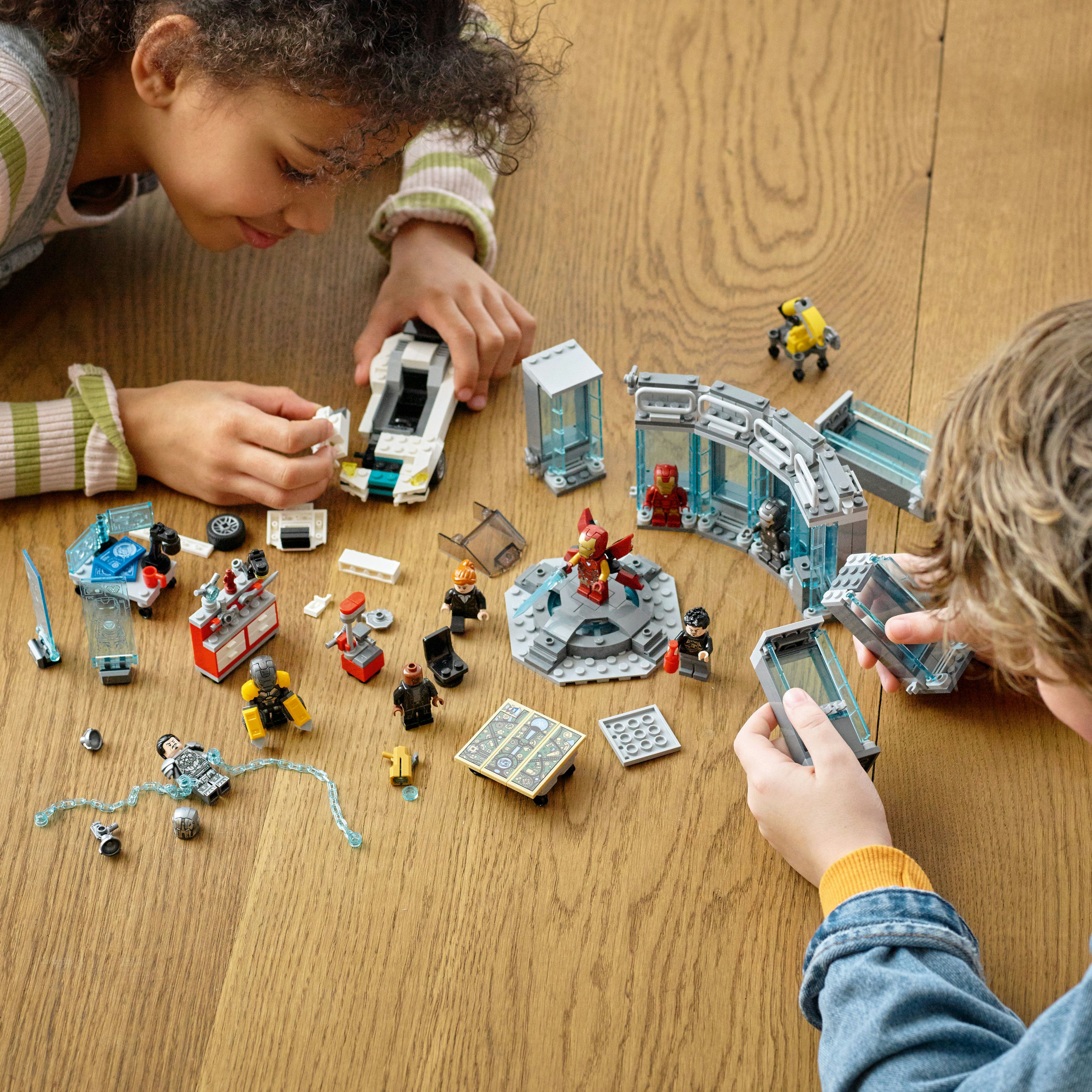 Dos niños juegan con sets de Lego, construyendo varias estructuras y ensamblando minifiguras en una mesa de madera.
