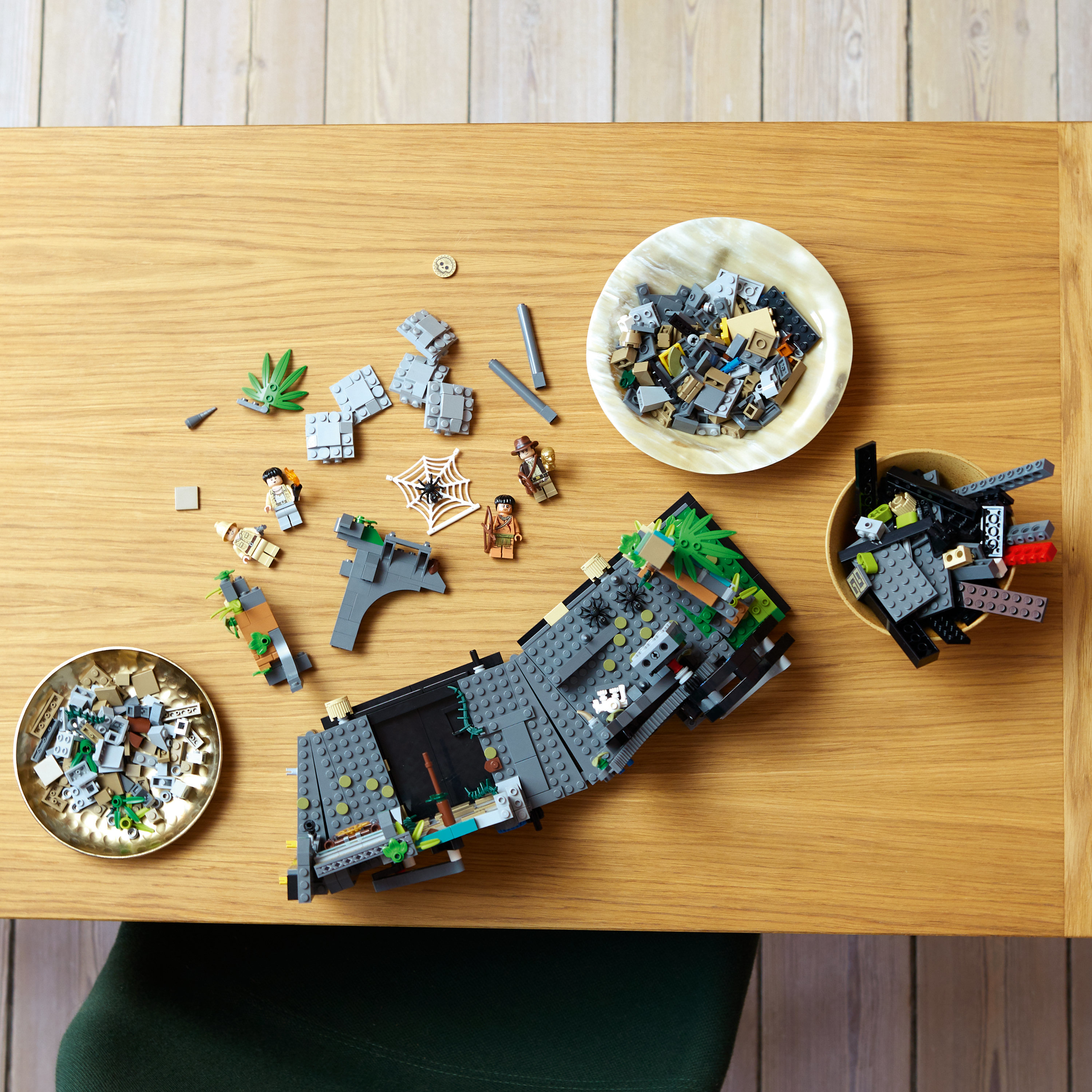 Lego-Teile auf einem Holztisch verstreut. Beinhaltet Minifiguren und zusammengebaute Struktur.