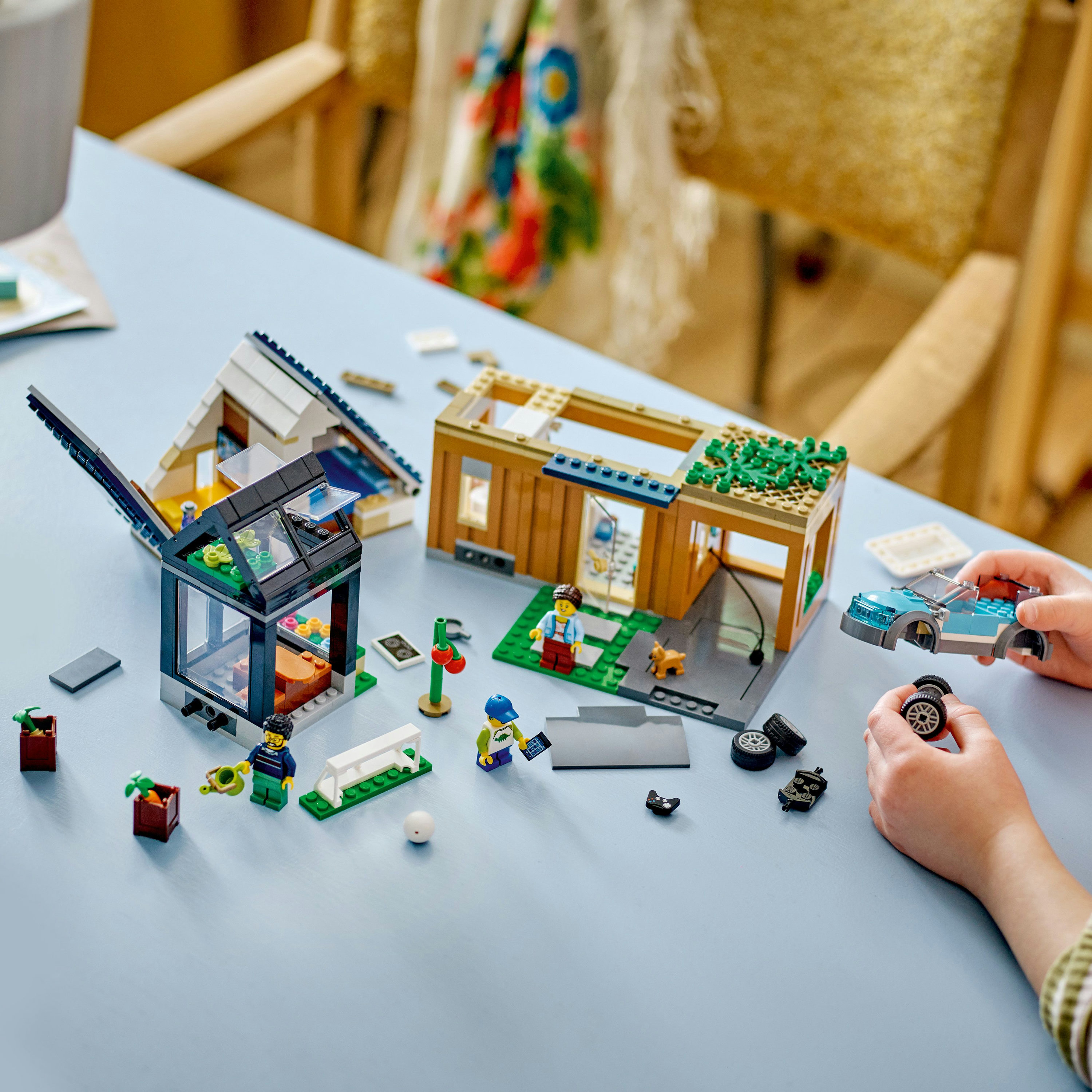 Lego-Set mit Häusern und Figuren. Die Szene spielt auf einem blauen Tisch mit Lego-Teilen.