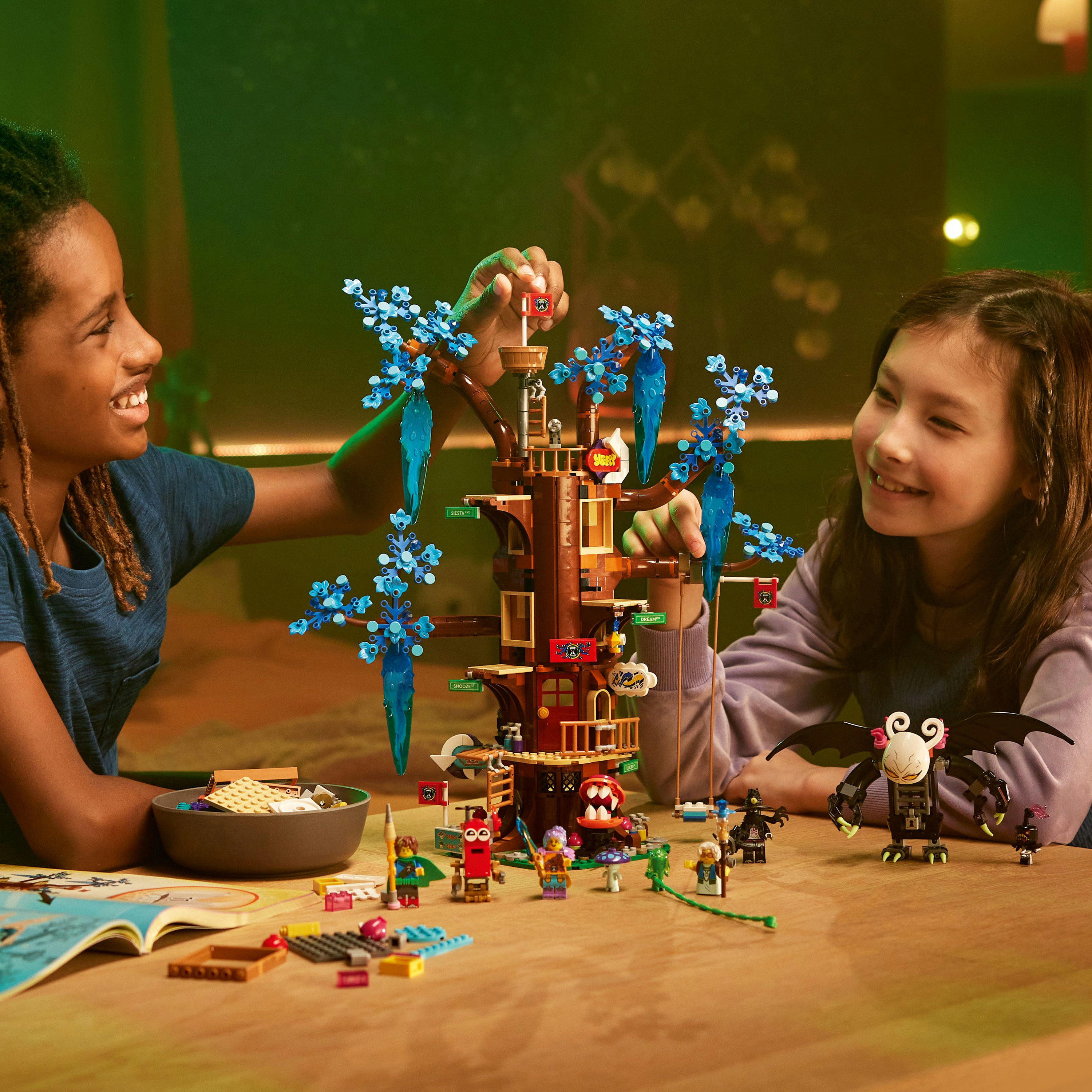 İki çocuk bir LEGO ağaç ev inşa ediyor. LEGO figürleri ve çeşitli LEGO tuğlaları ahşap bir masada.