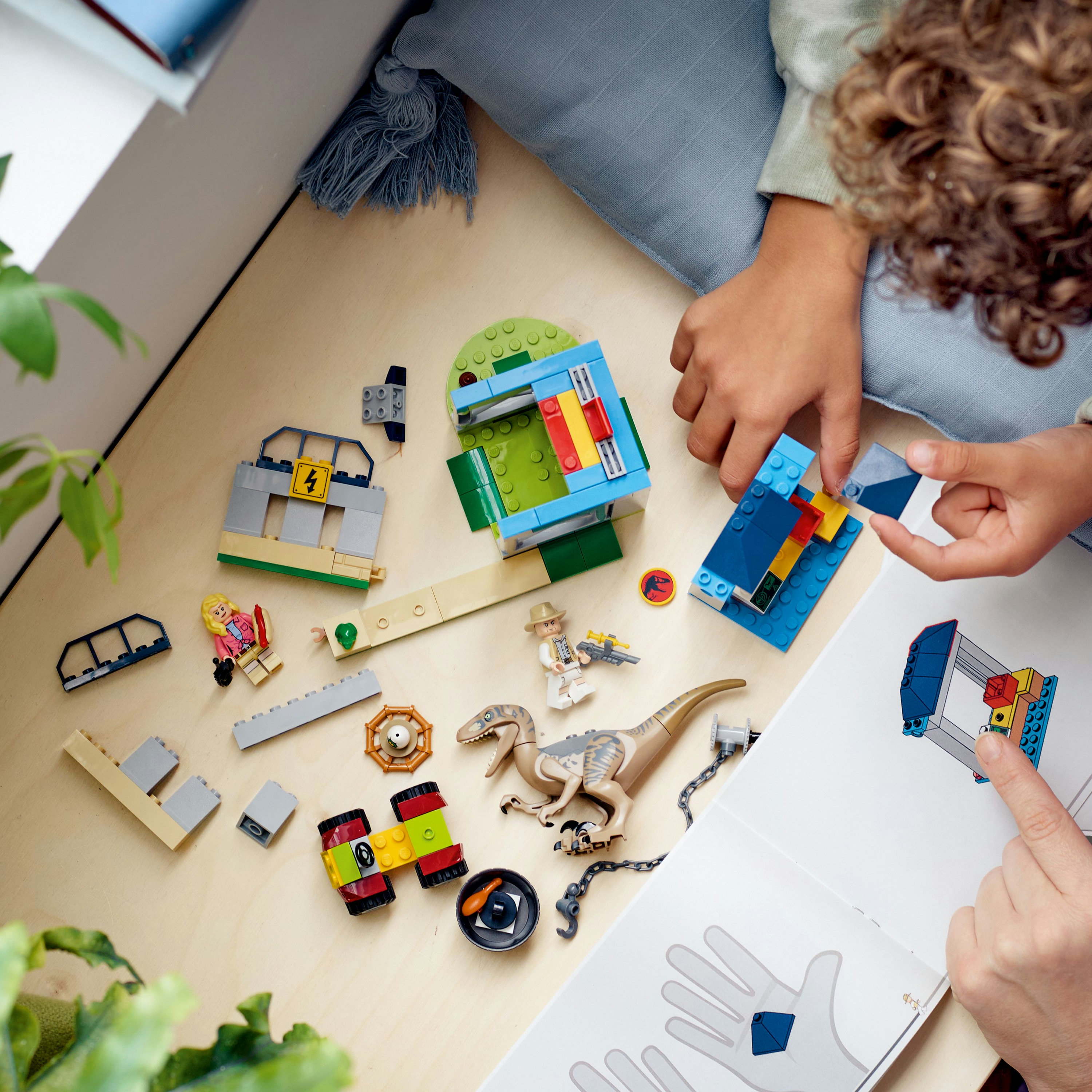 Kind, das ein Lego-Set mit Dinosaurier, Bauteilen und Figuren auf einer Holzoberfläche zusammenbaut.
