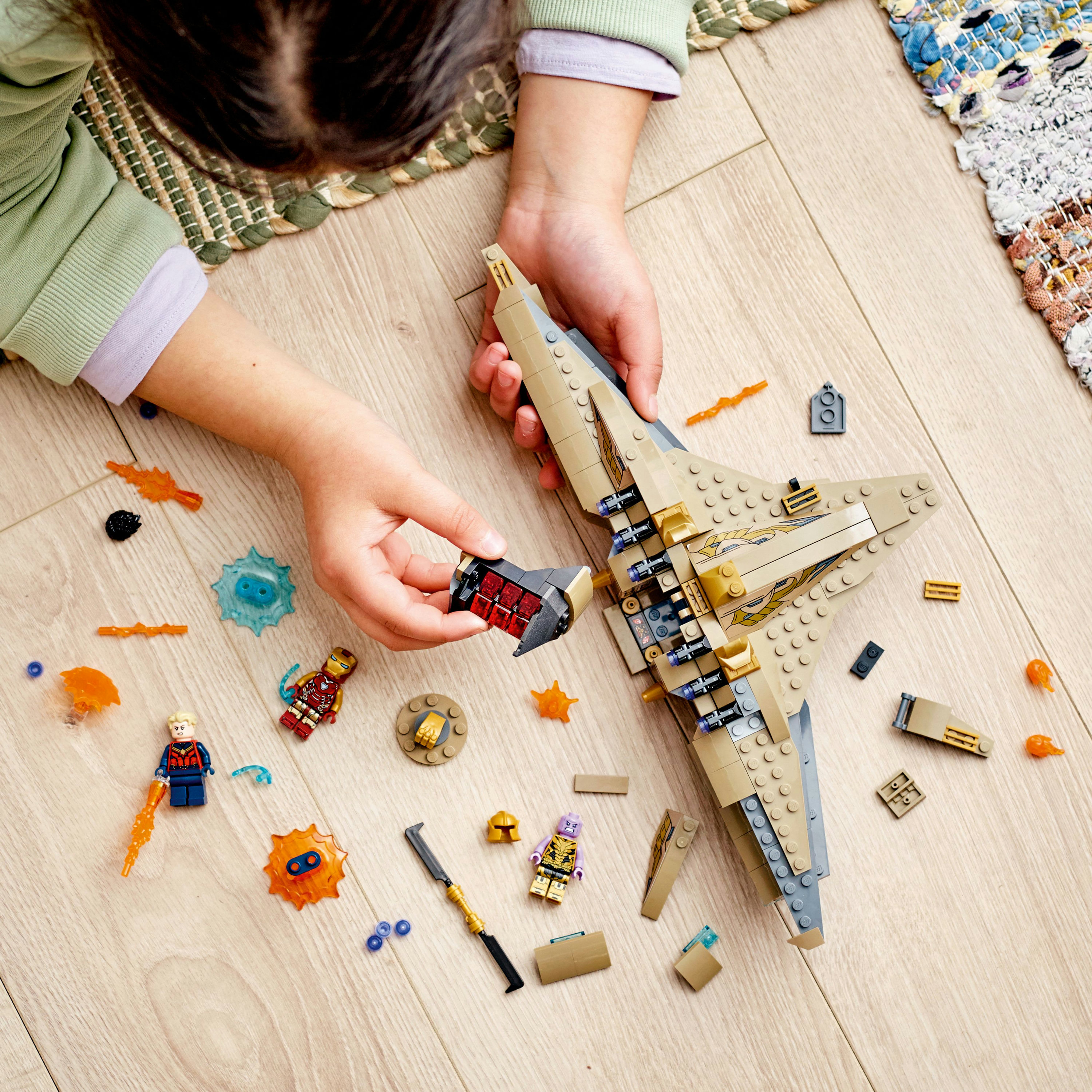 Child assembling a Lego set with a tan aircraft and mini-figures on a wooden surface. Includes action parts.