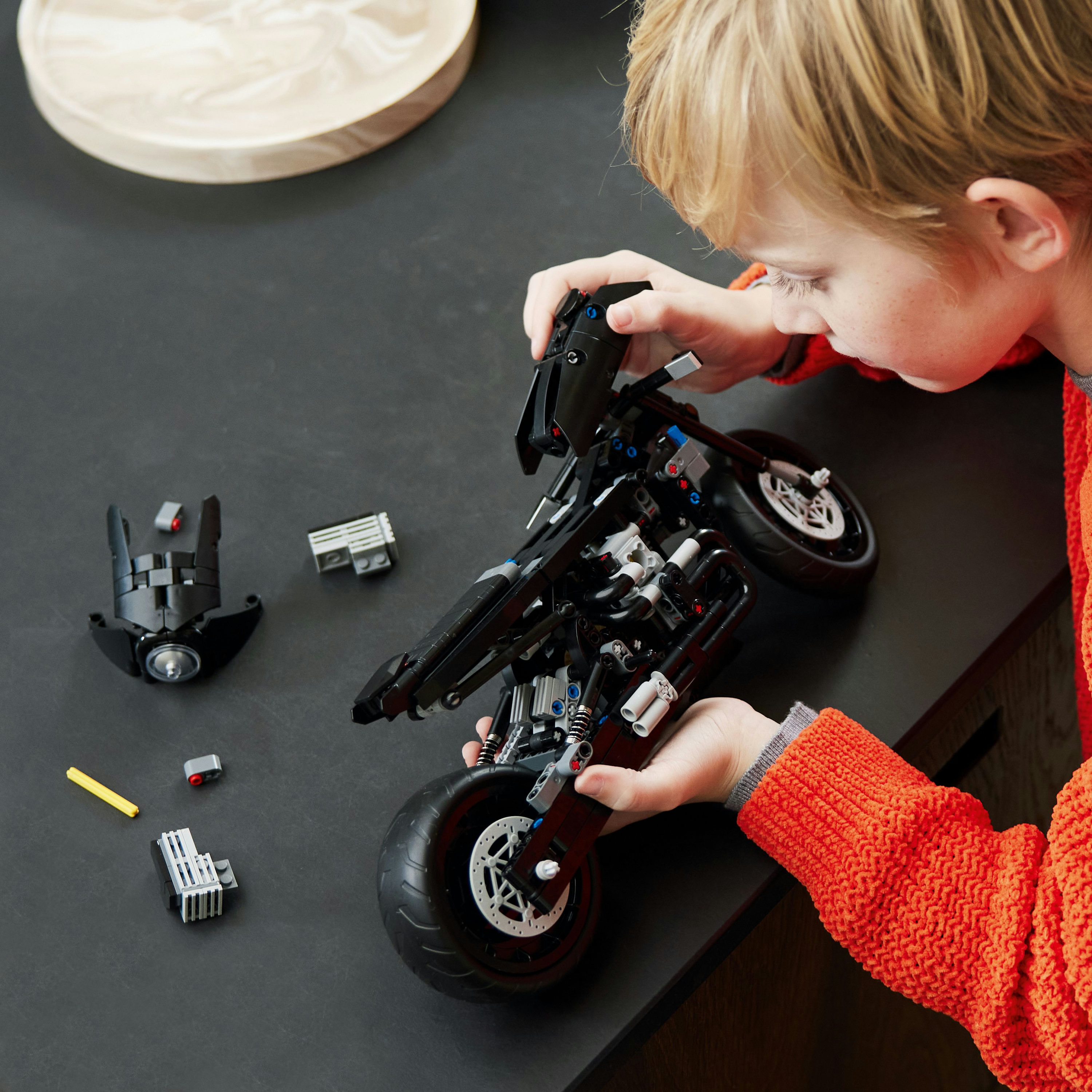 Een kind dat een zwarte Lego motorfiets in elkaar zet, met verschillende Lego-onderdelen eromheen.