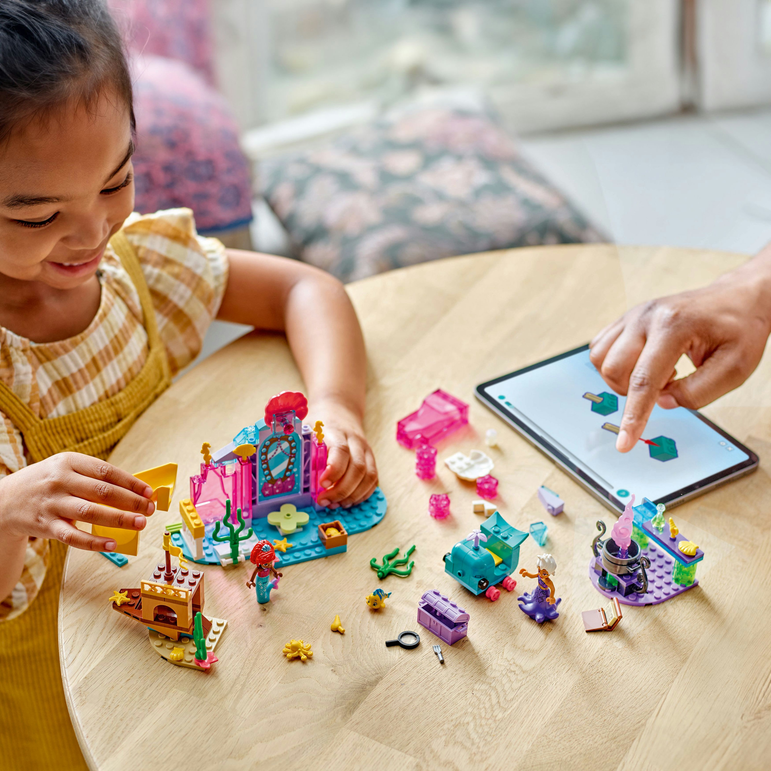 Dziewczynka i ręce bawiące się zestawem Lego na drewnianym stole. Widoczna syrena i zamek.