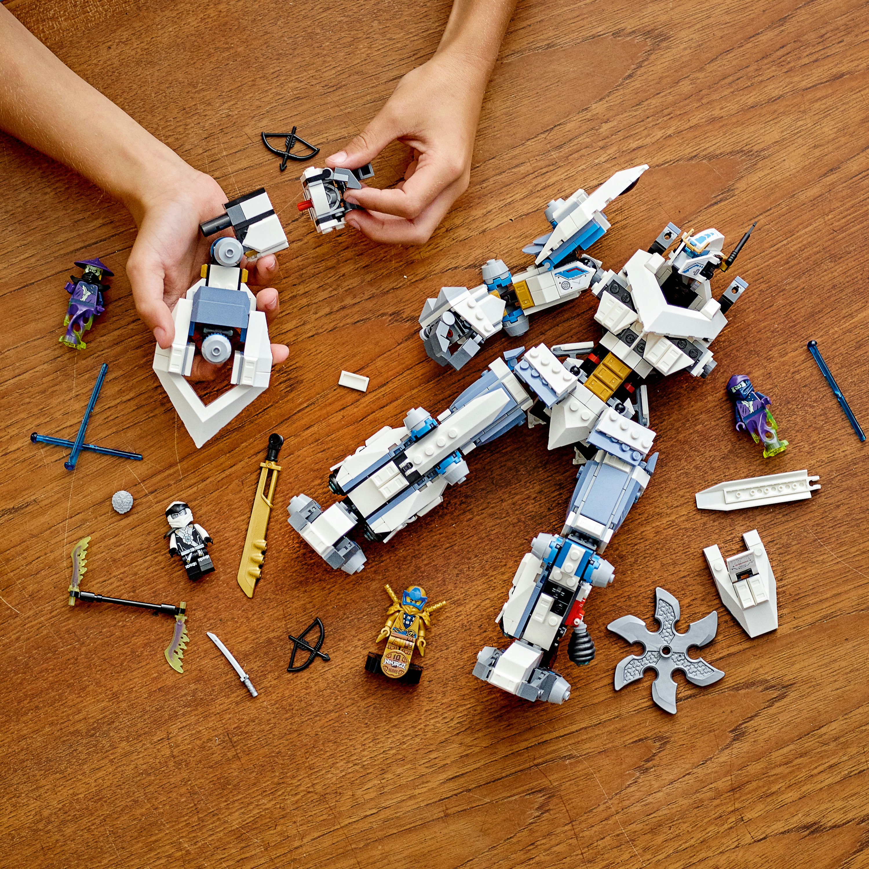 Kind baut Lego Ninjago Roboter zusammen. Der Roboter ist weiß und blau mit Waffen. Holz Hintergrund.