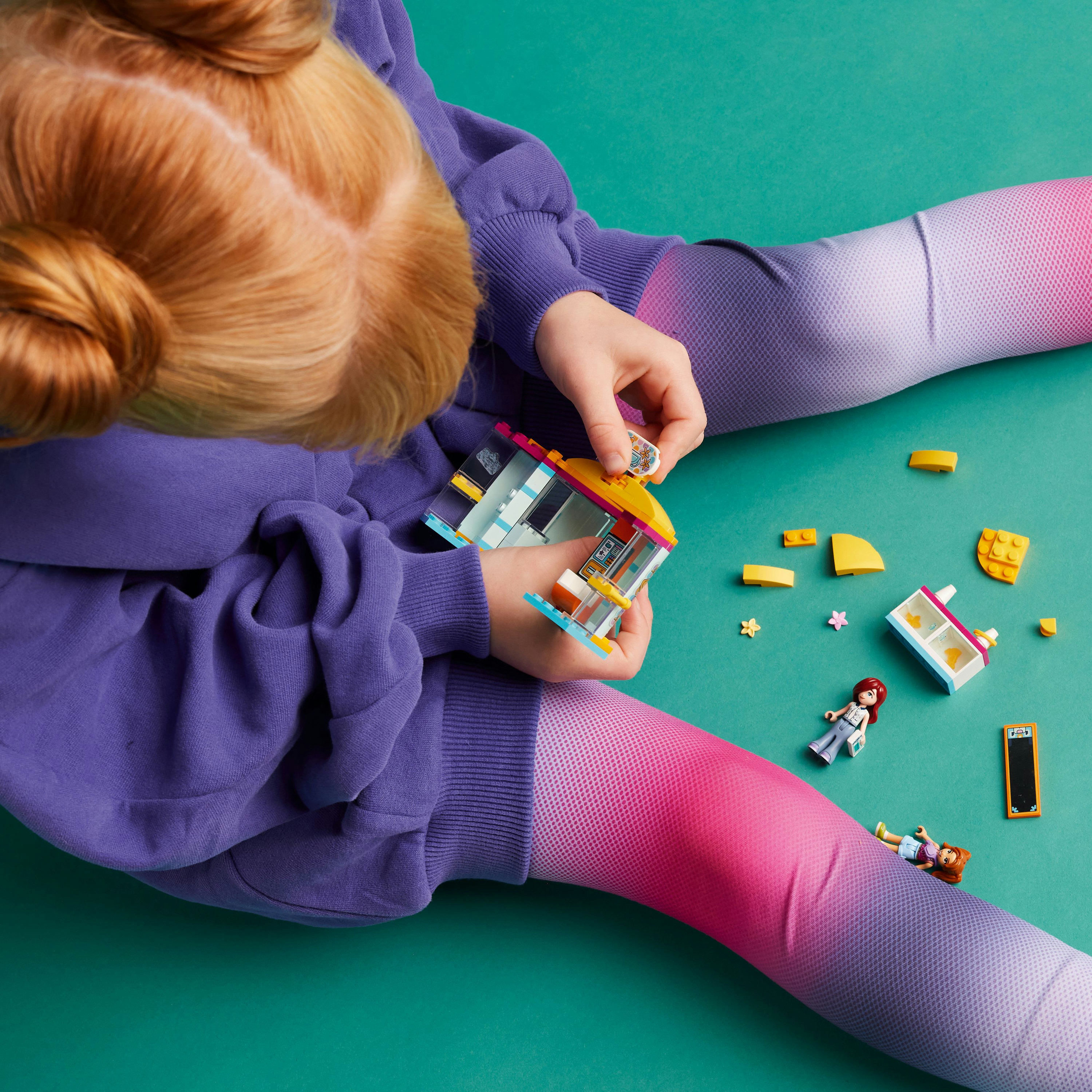 Ein Kind, das ein Lego-Haus-Set auf einer grünen Oberfläche zusammenbaut, mit Miniaturfiguren und anderen Legoteilen.