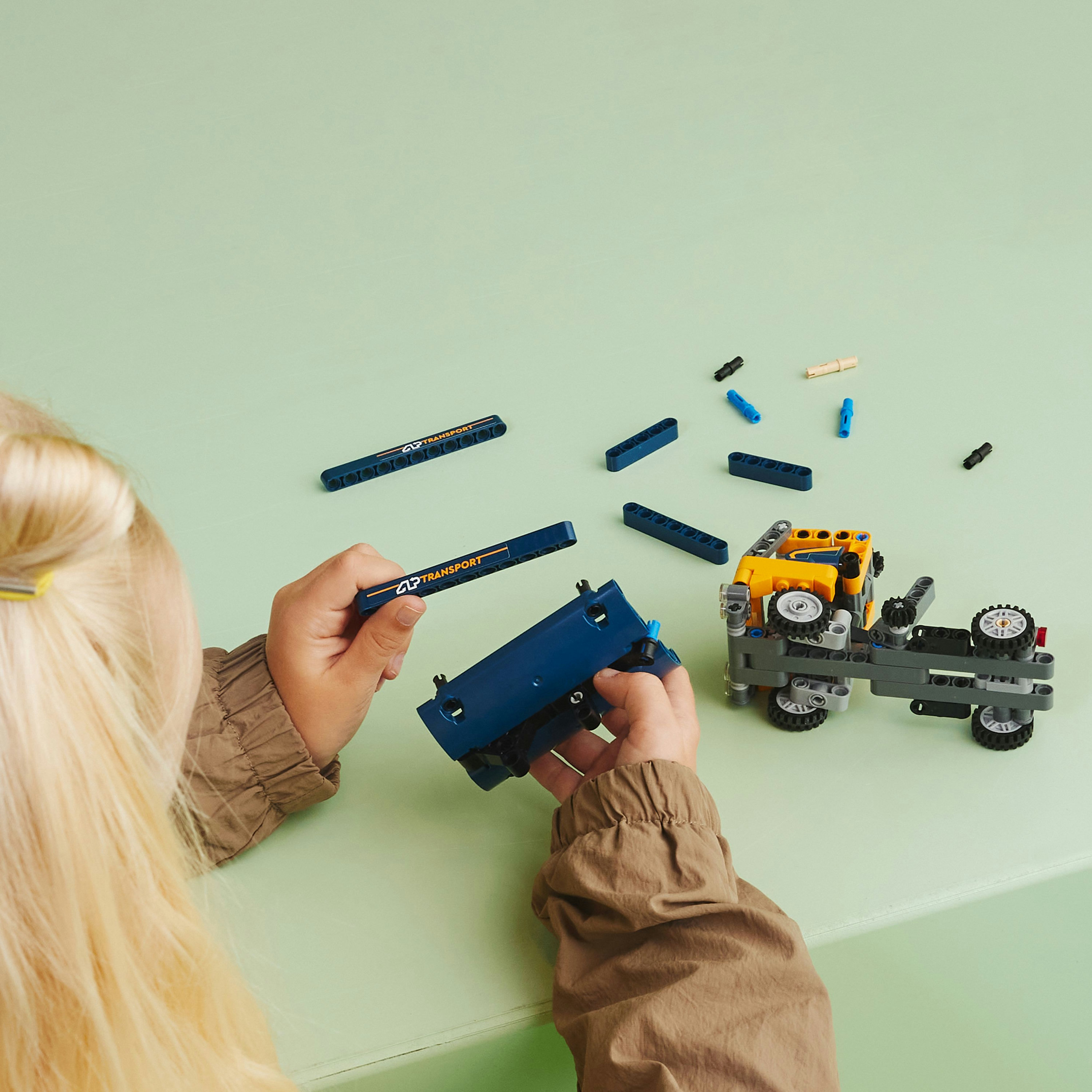 Un niño montando un set Lego Technic con piezas de construcción azules sobre una mesa verde claro.