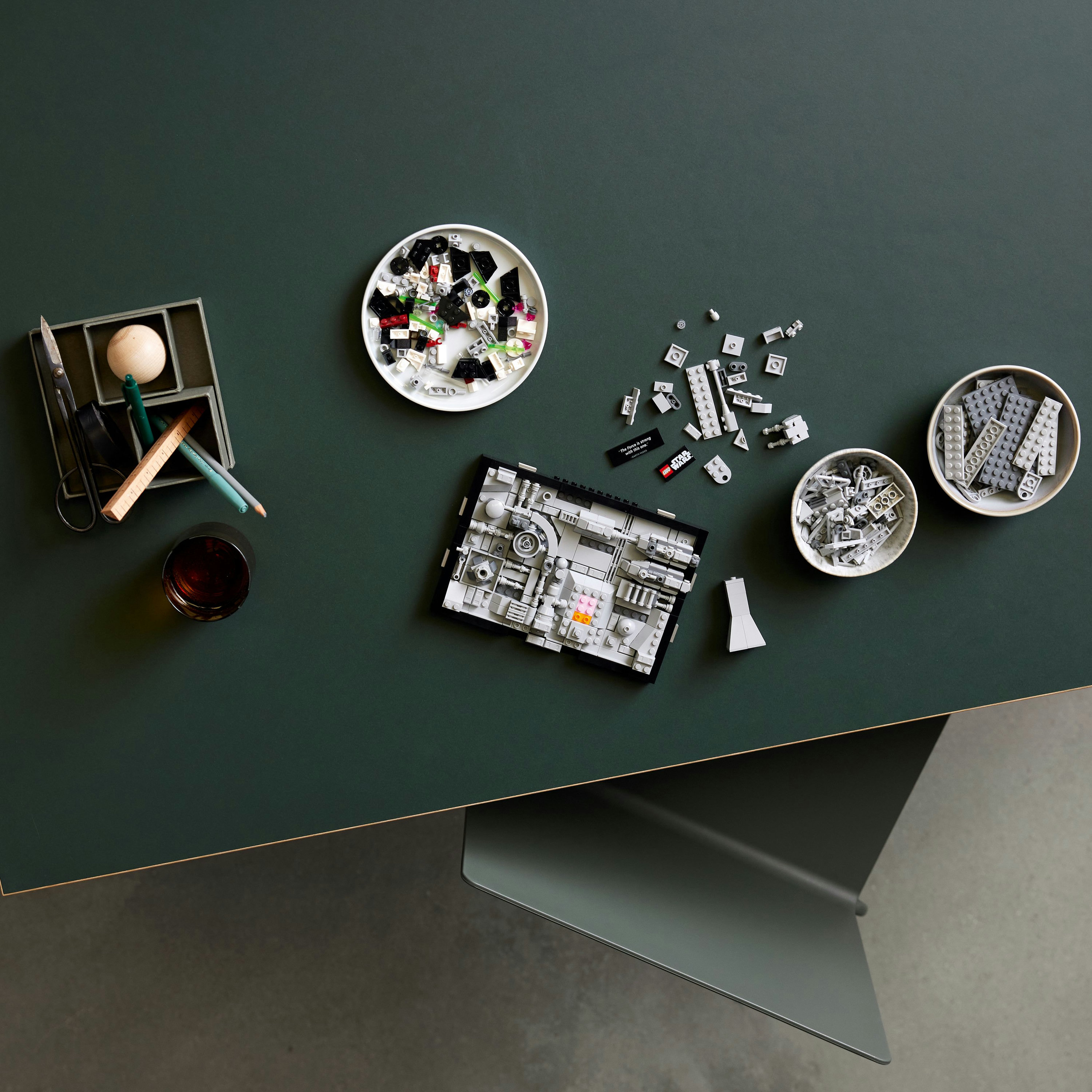 Widok z góry na zielony stół z Lego, narzędziami i szklanką napoju.