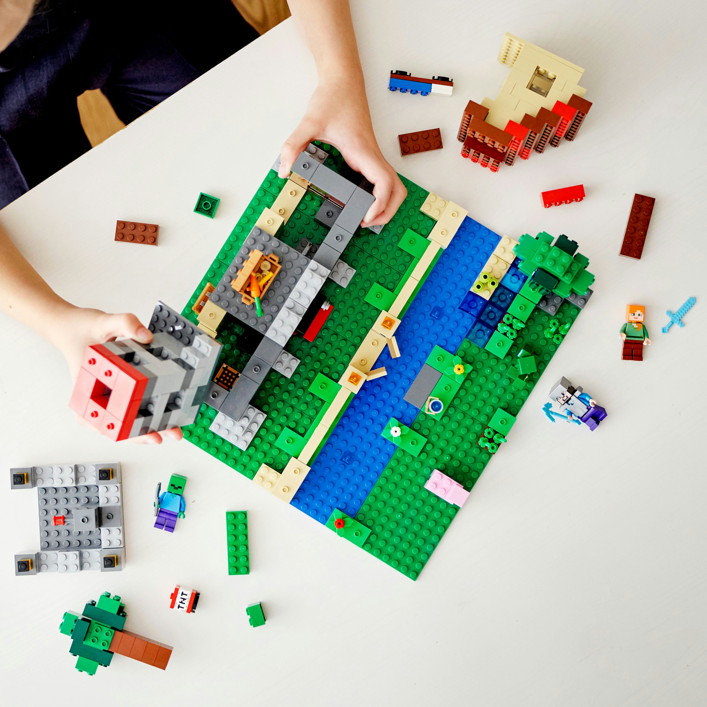 Un bambino che costruisce con i mattoncini Lego su un tavolo bianco, costruendo un paesaggio.