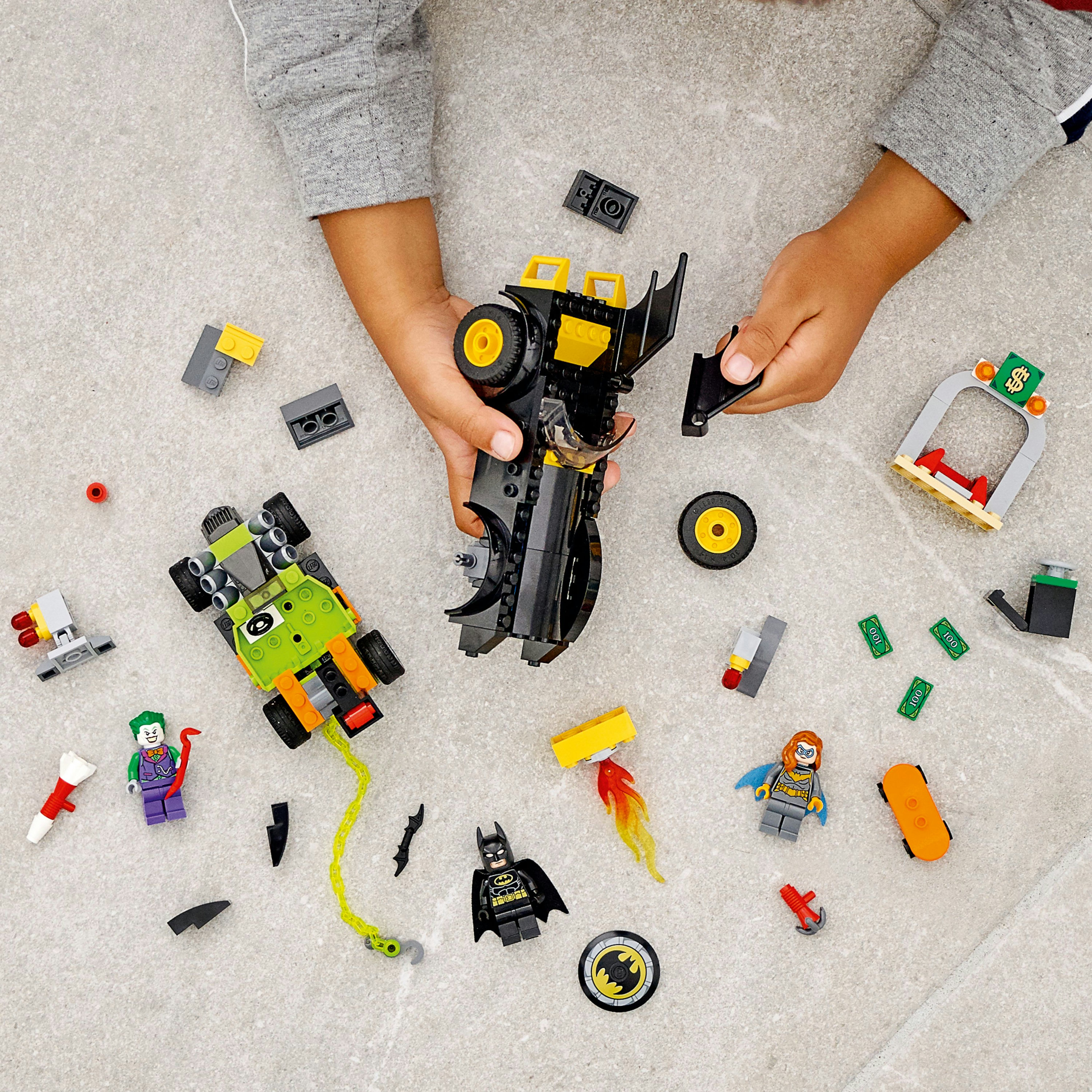 Dziecko bawi się zestawem LEGO Batman. Zawiera Batmana, Jokera i Batmobil. Kilka klocków LEGO jest rozrzuconych.