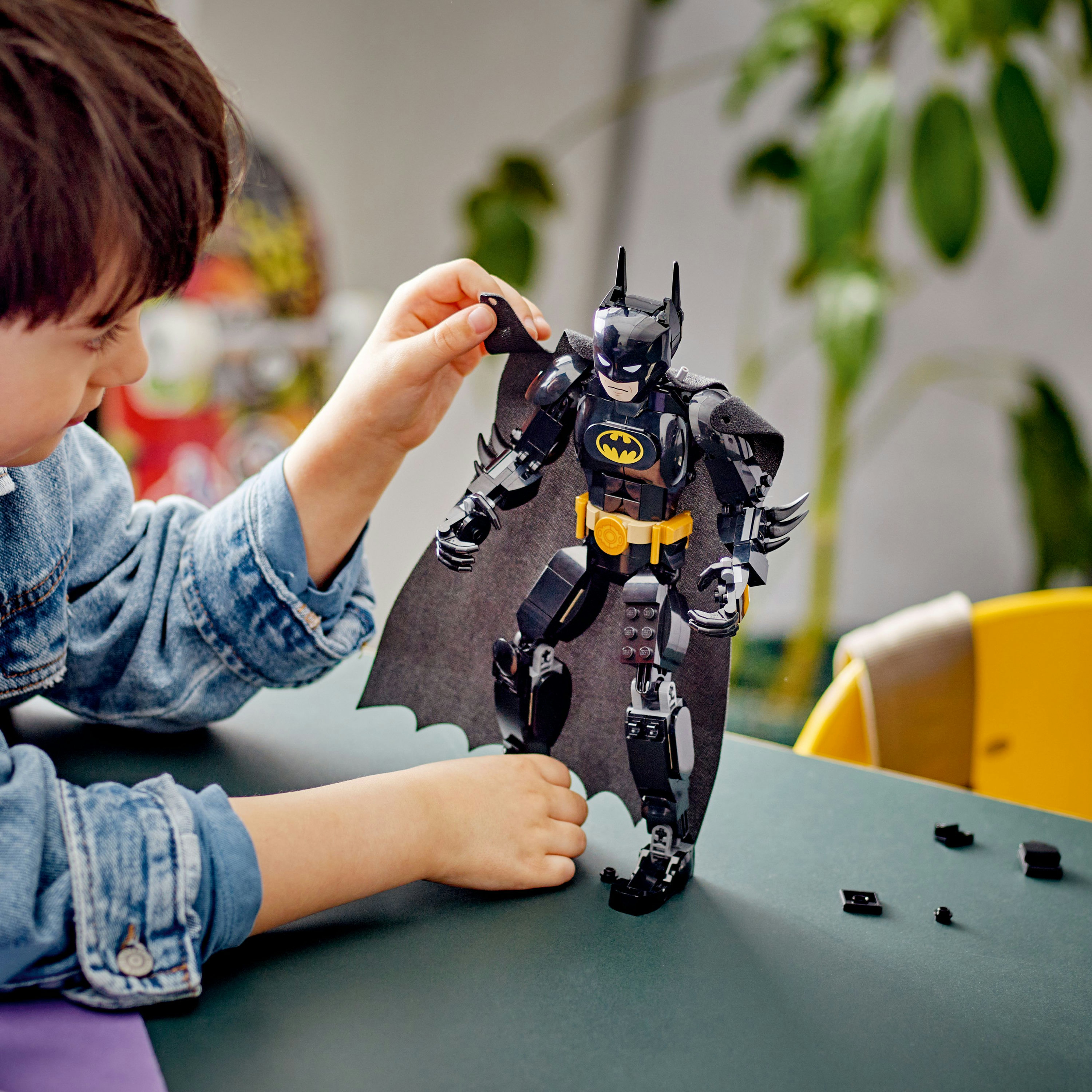 Un niño construyendo una figura de LEGO Batman. La figura es negra con cinturón y capa amarillos.