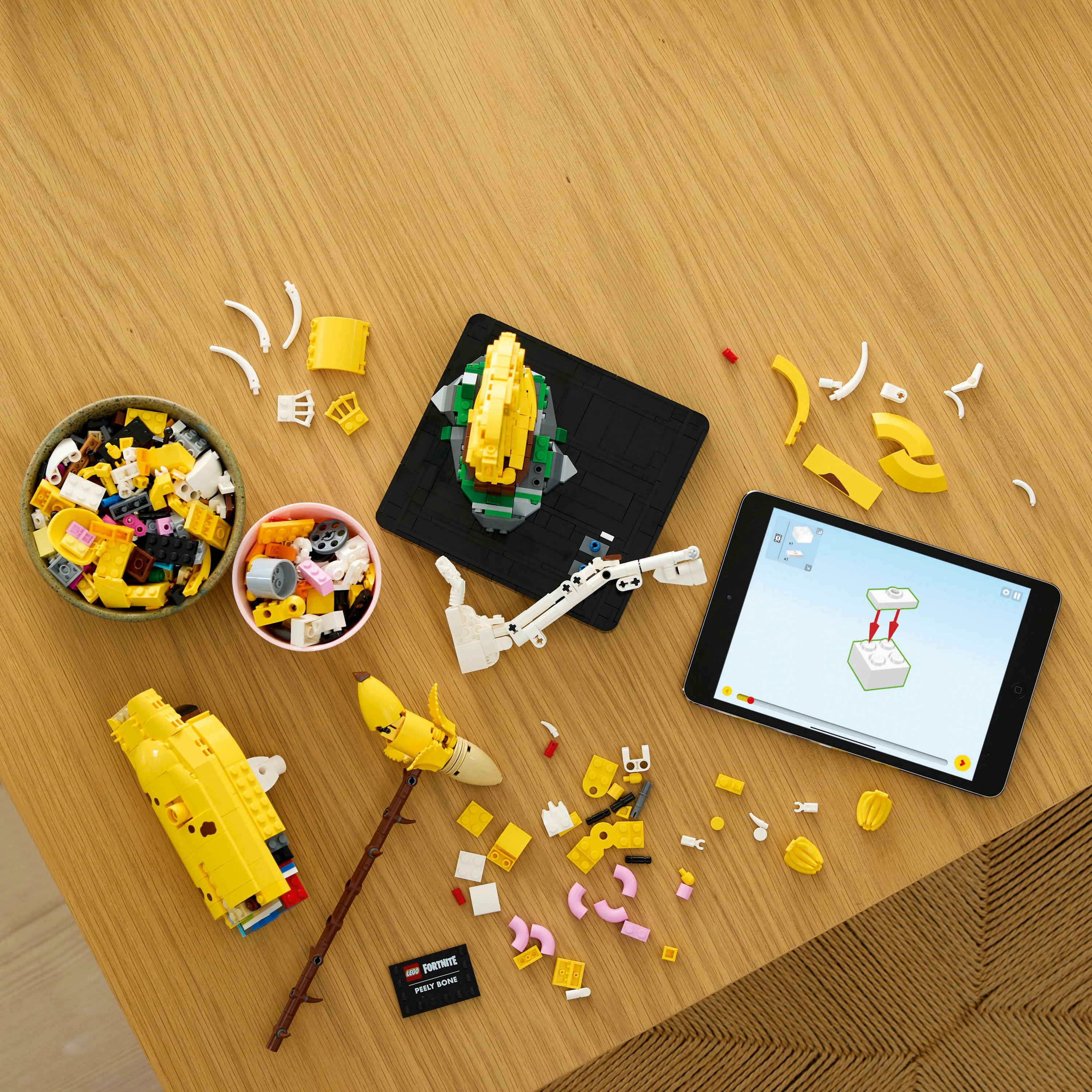 Lego-Teile und ein Tablet mit Anweisungen liegen auf einem Tisch. Verschiedene Lego-Komponenten und Schalen sind ebenfalls vorhanden.