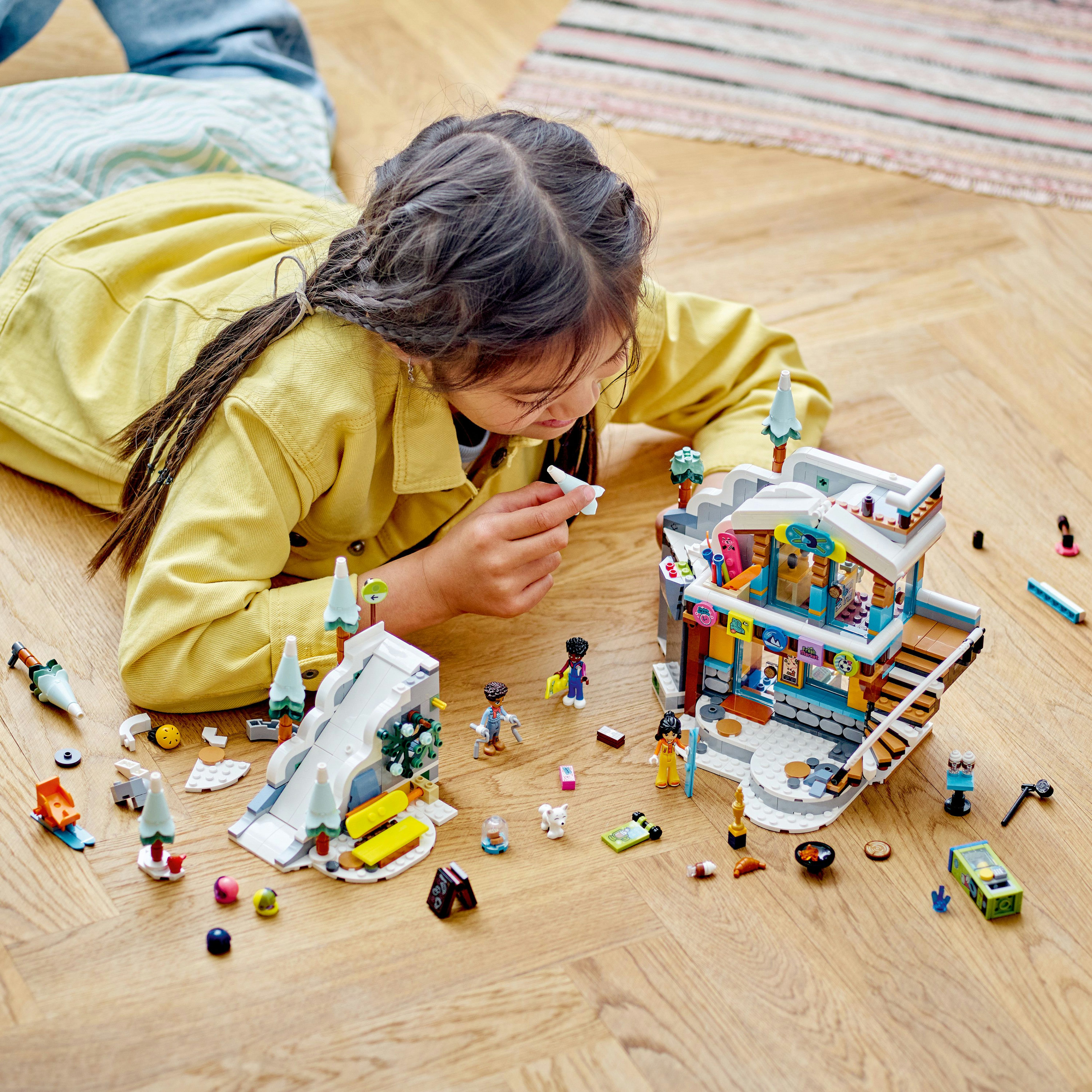 Una niña juega con un set LEGO Friends de estación de esquí en un suelo de madera.