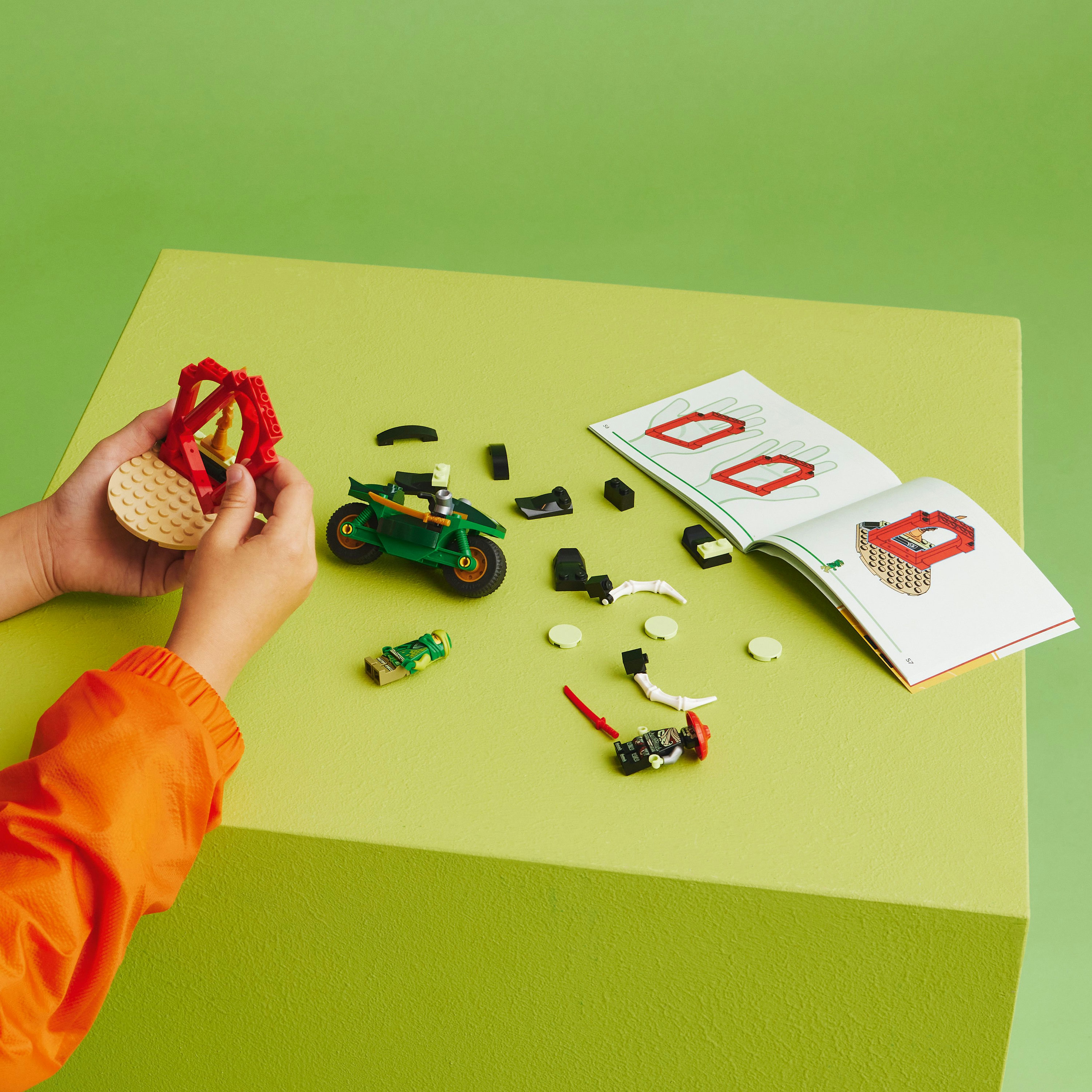 Lego motosikletini birleştiren eller, Lego tuğlaları ve talimat kılavuzu sayfalarıyla çevrili.