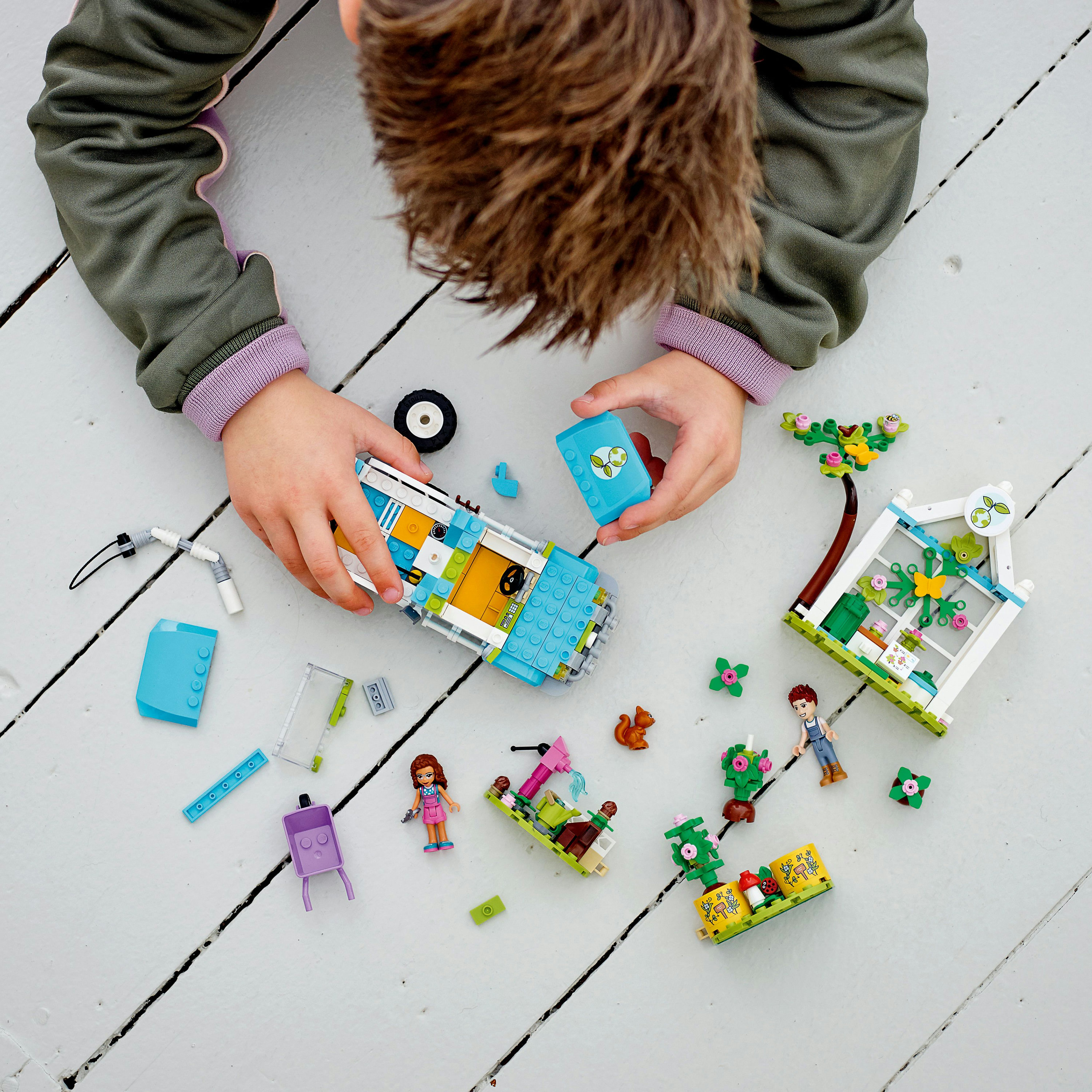 Ein Kind spielt mit Lego Friends, baut ein Auto, ein Haus und eine Gartenszene.