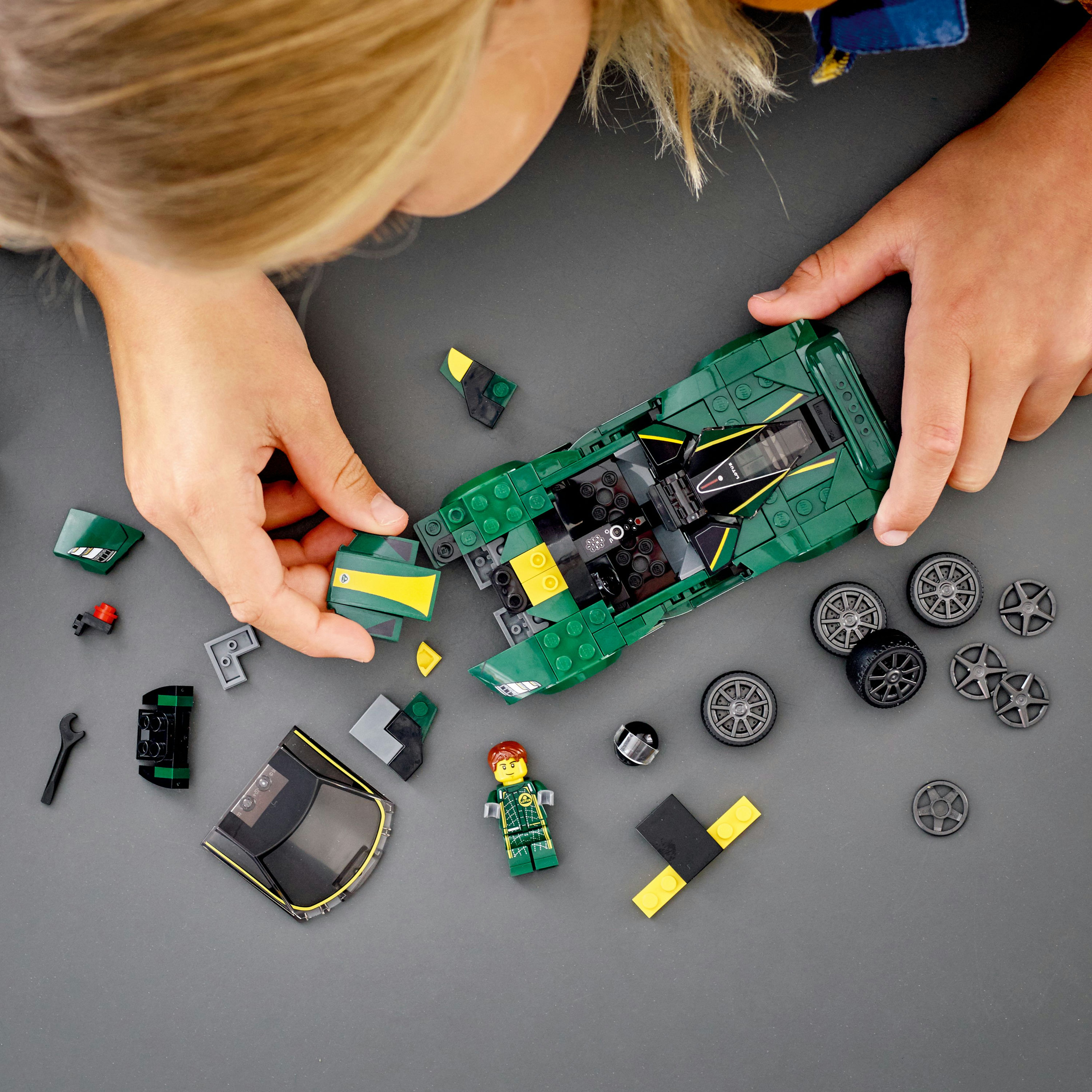 Ein Kind baut ein grünes Lego-Auto zusammen, verschiedene Teile sichtbar.