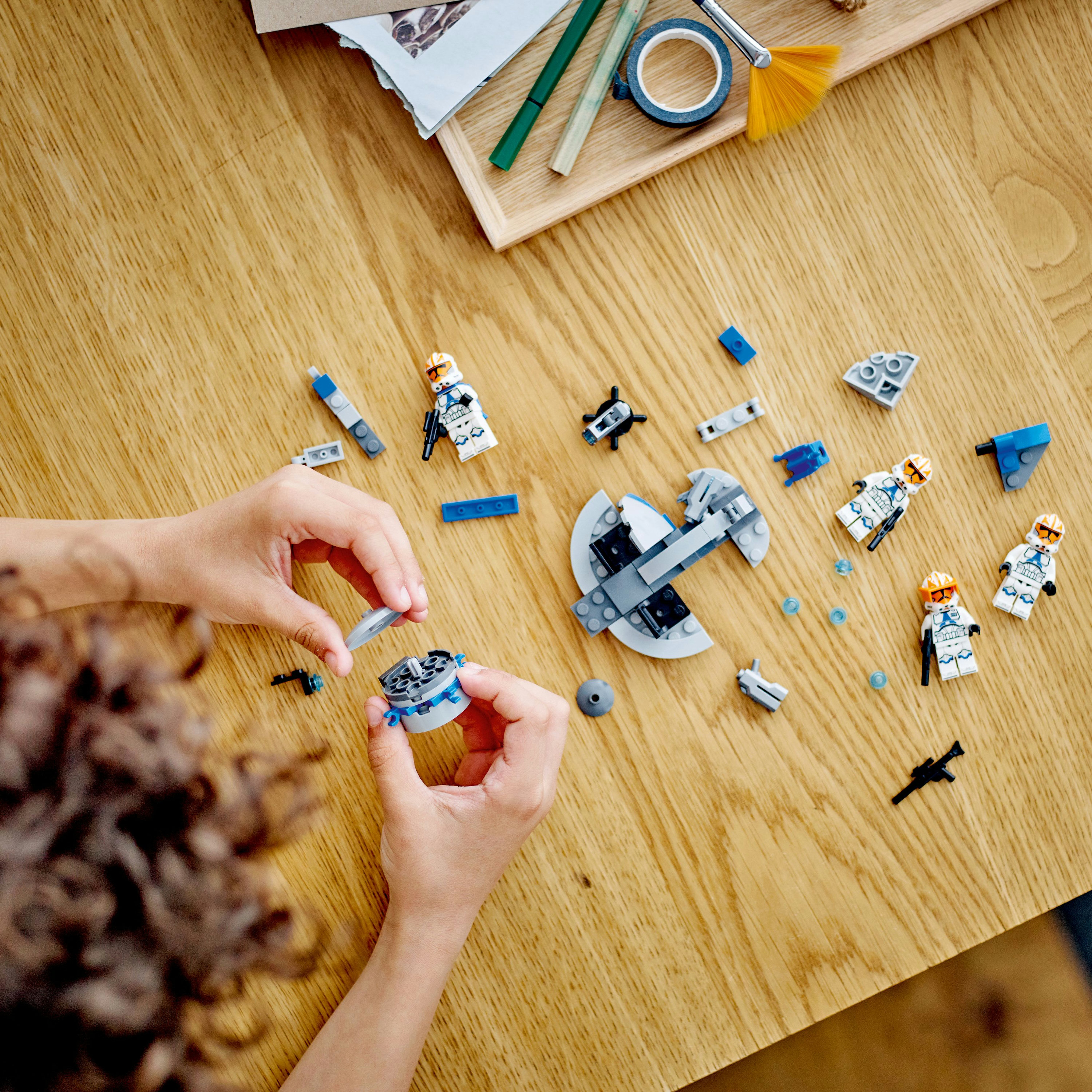Een kind bouwt een Lego-set met minifiguren en accessoires op een houten tafel.