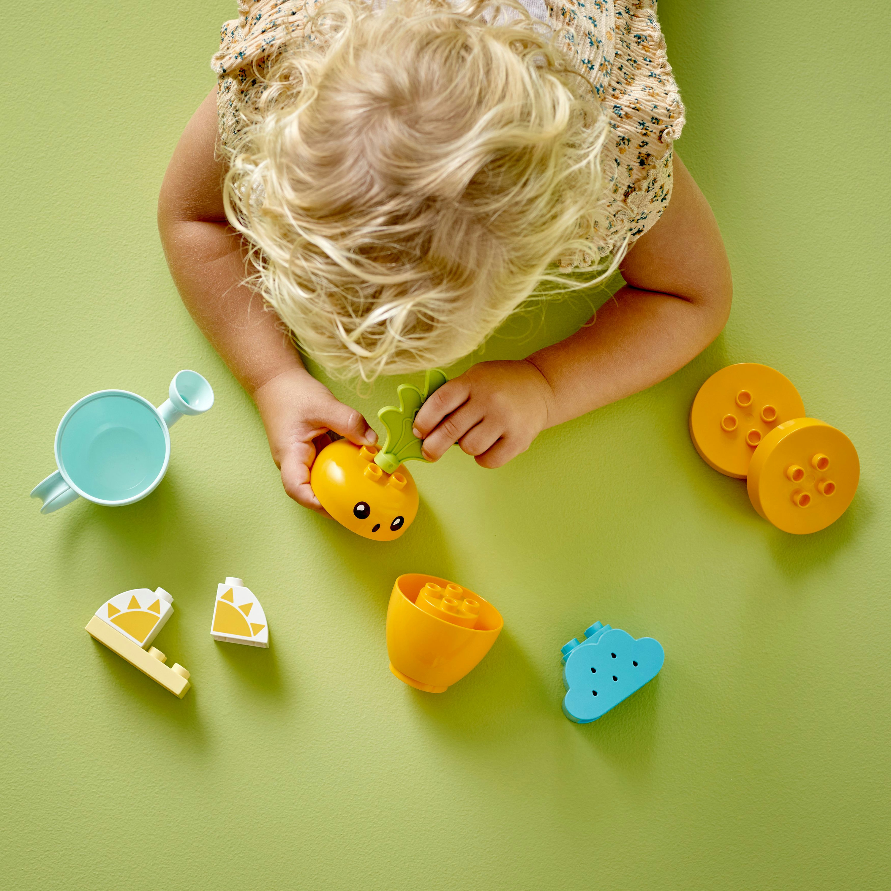Handen van een kind spelen met Lego-fruit en een blauwe gieter.