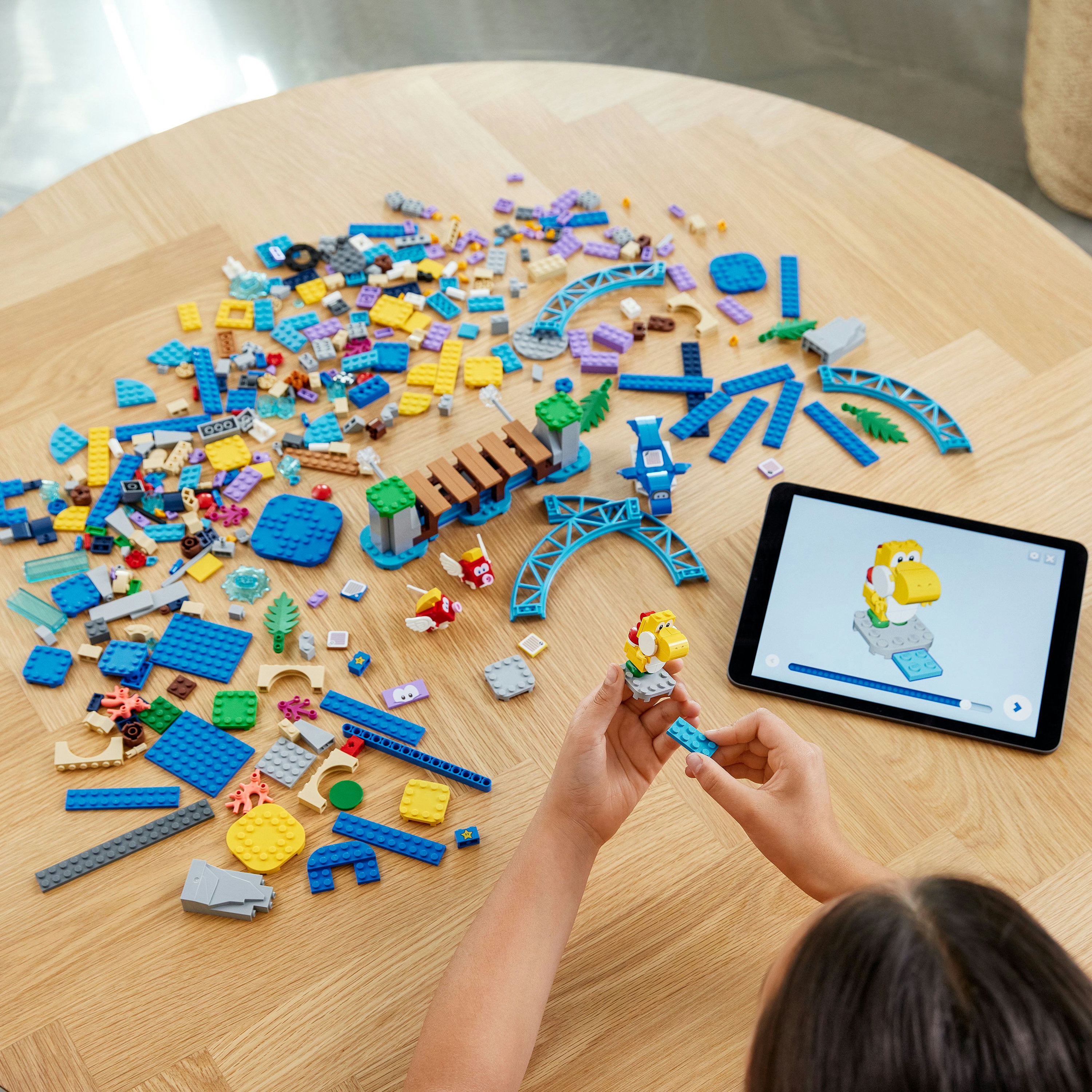 Ein Kind baut mit LEGO-Steinen auf einem Holztisch, mit einem Tablet, das Anweisungen zeigt.
