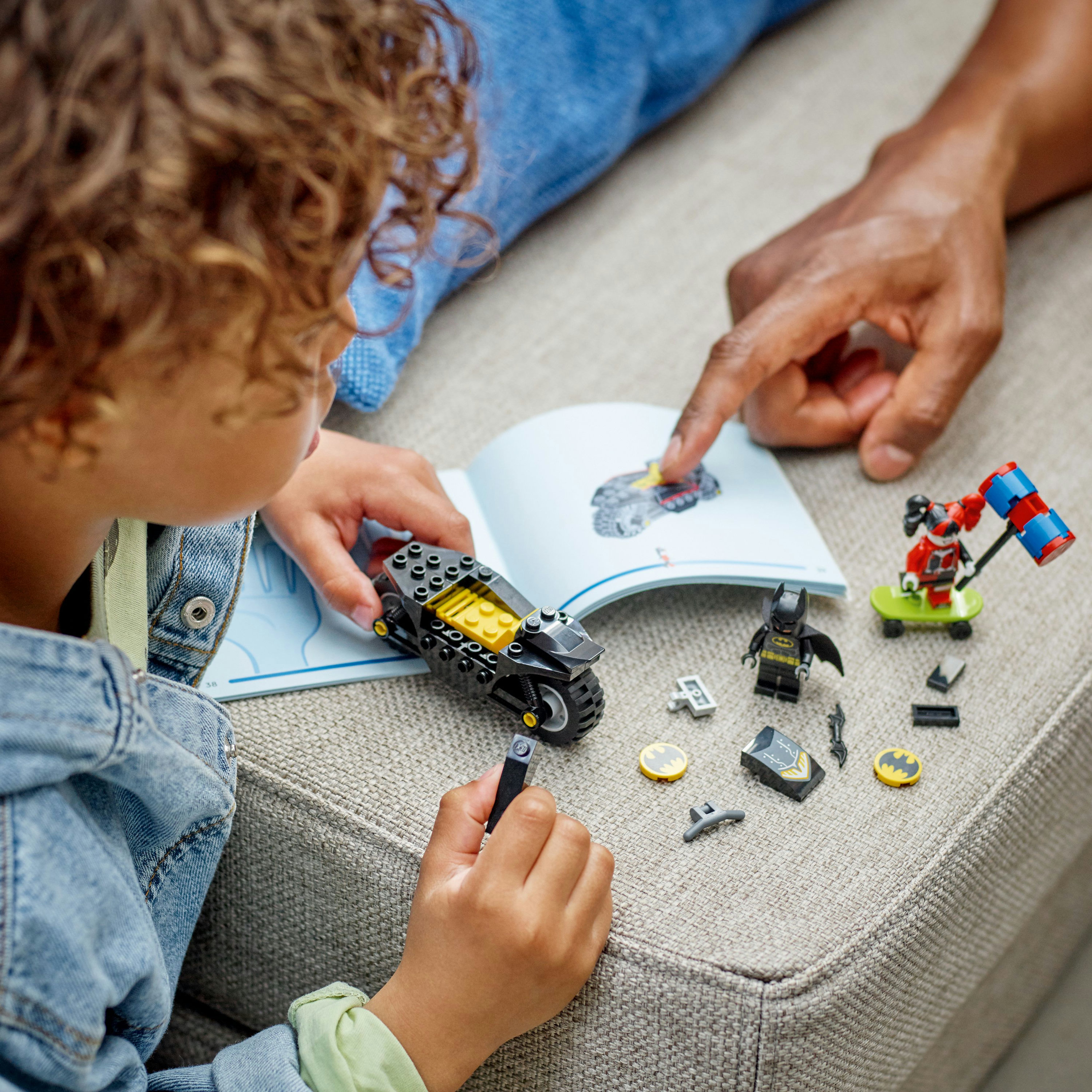 Ein Kind baut mit Anleitung ein Lego-Set. Das Set enthält ein schwarzes Motorrad, Batman und weiteres Zubehör.