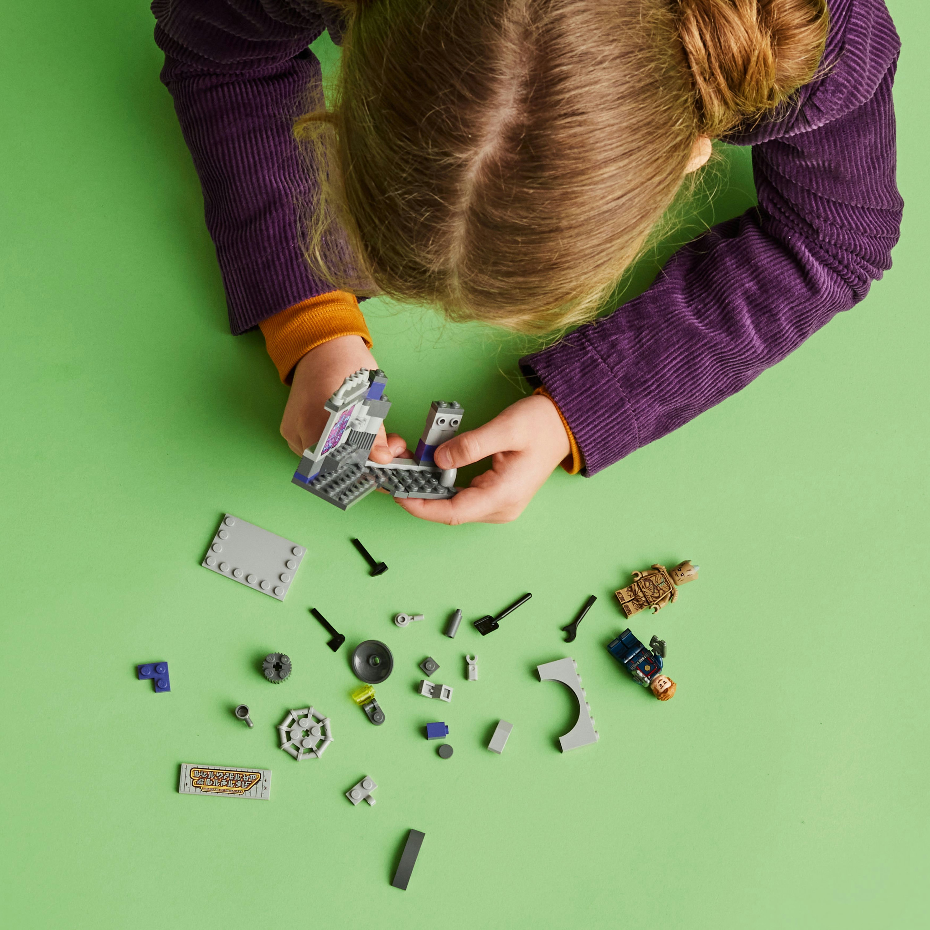 Een kind speelt met Lego-stenen op een groen oppervlak. Veel stenen zijn verspreid, met figuren.