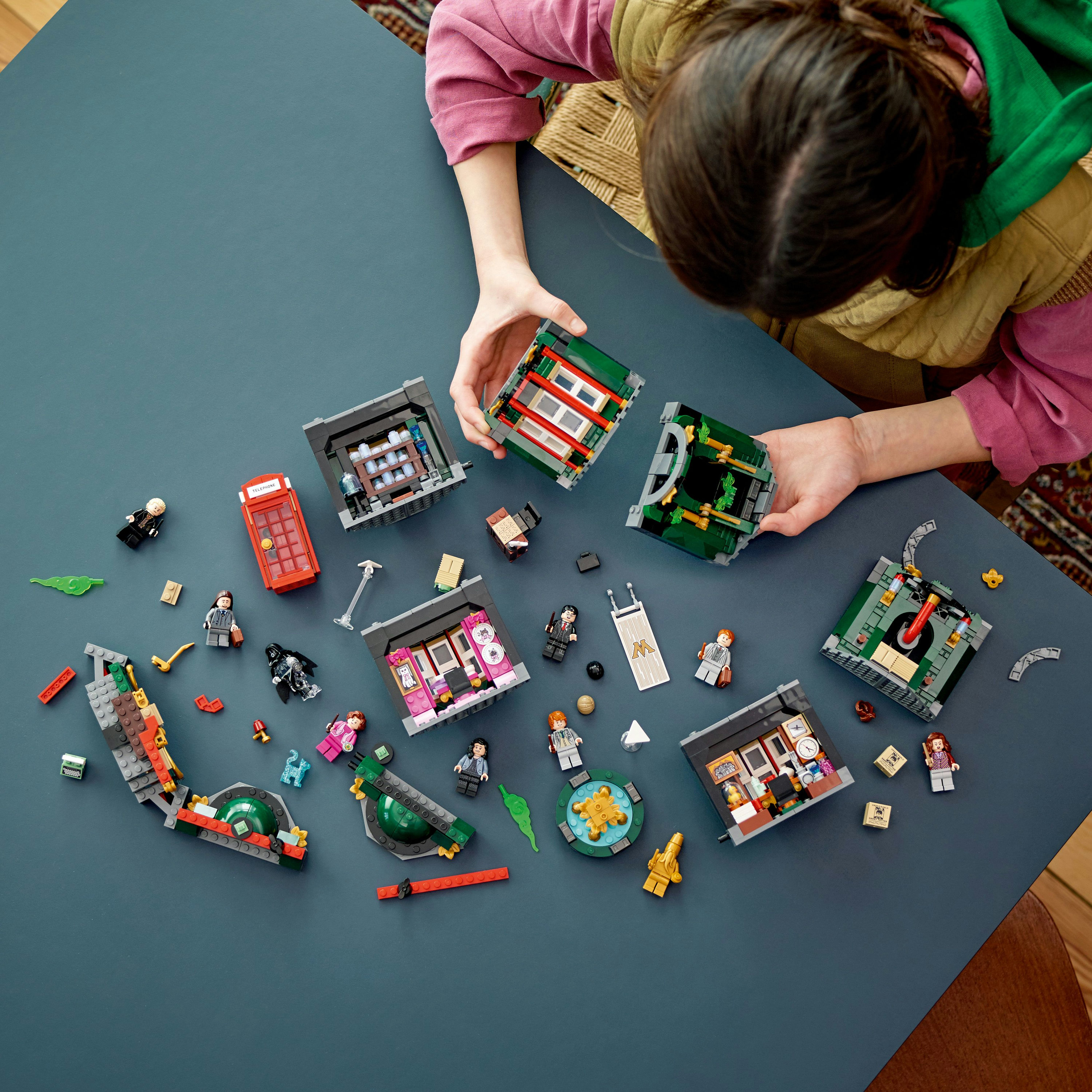 Ein Kind interagiert mit LEGO Harry Potter Sets auf einem blauen Tisch, umgeben von verstreuten Teilen und Figuren.