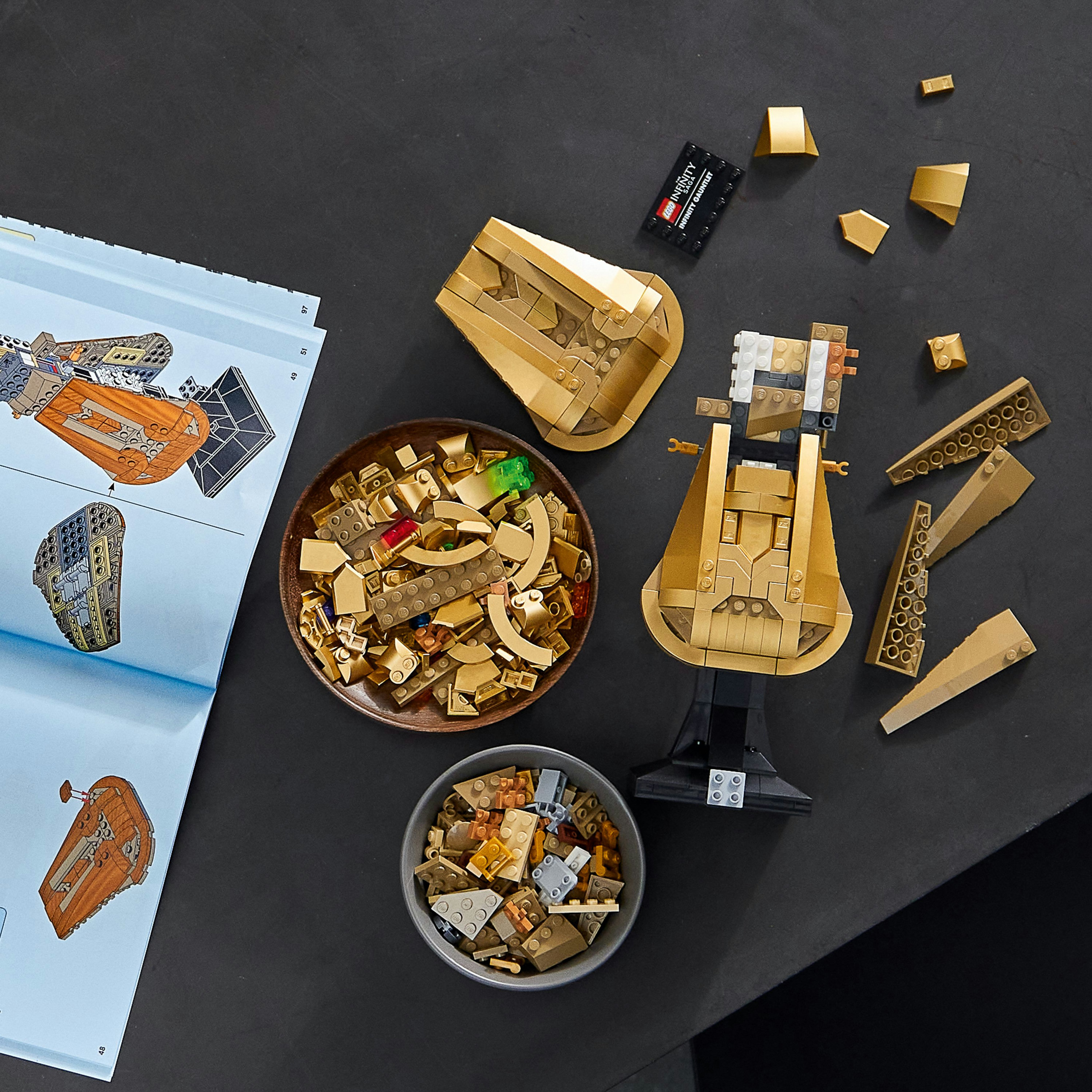 Elementy zestawu LEGO, w tym złote elementy i instrukcje, są rozmieszczone na czarnej powierzchni.