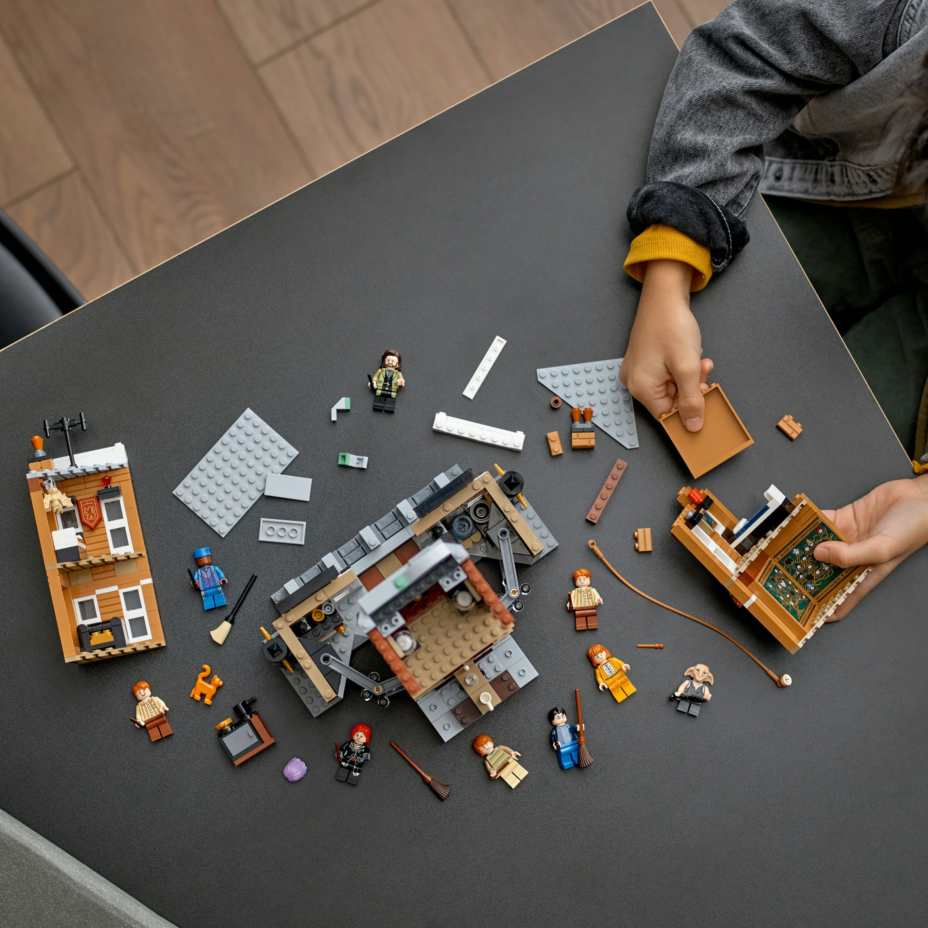 Lego-Set auf einem Tisch mit Bauteilen und Minifiguren. Kinderhände interagieren mit Teilen.