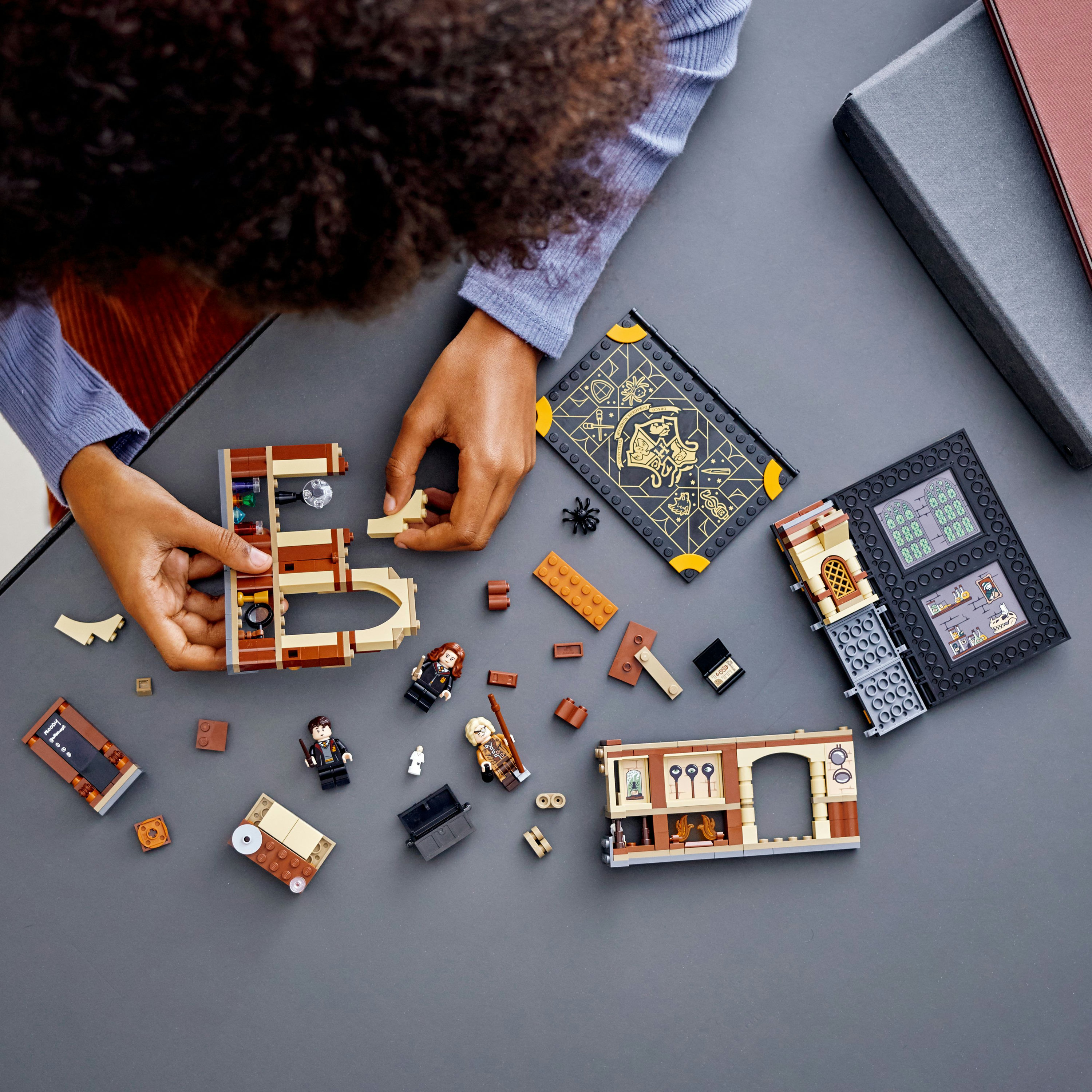 Hände, die Lego-Teile zusammensetzen. Verschiedene Lego-Komponenten und Mini-Figuren sind verstreut.