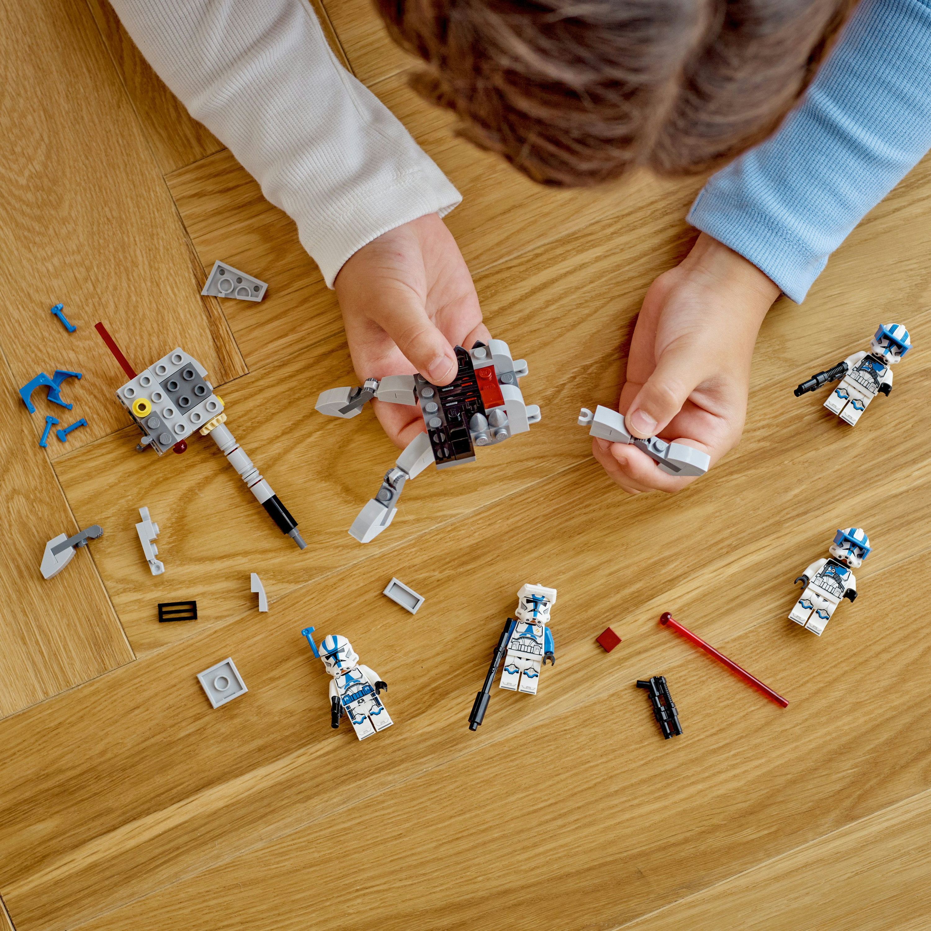 Ein Kind spielt mit Lego. Lego-Figuren und Teile liegen verstreut auf einem Holzboden.