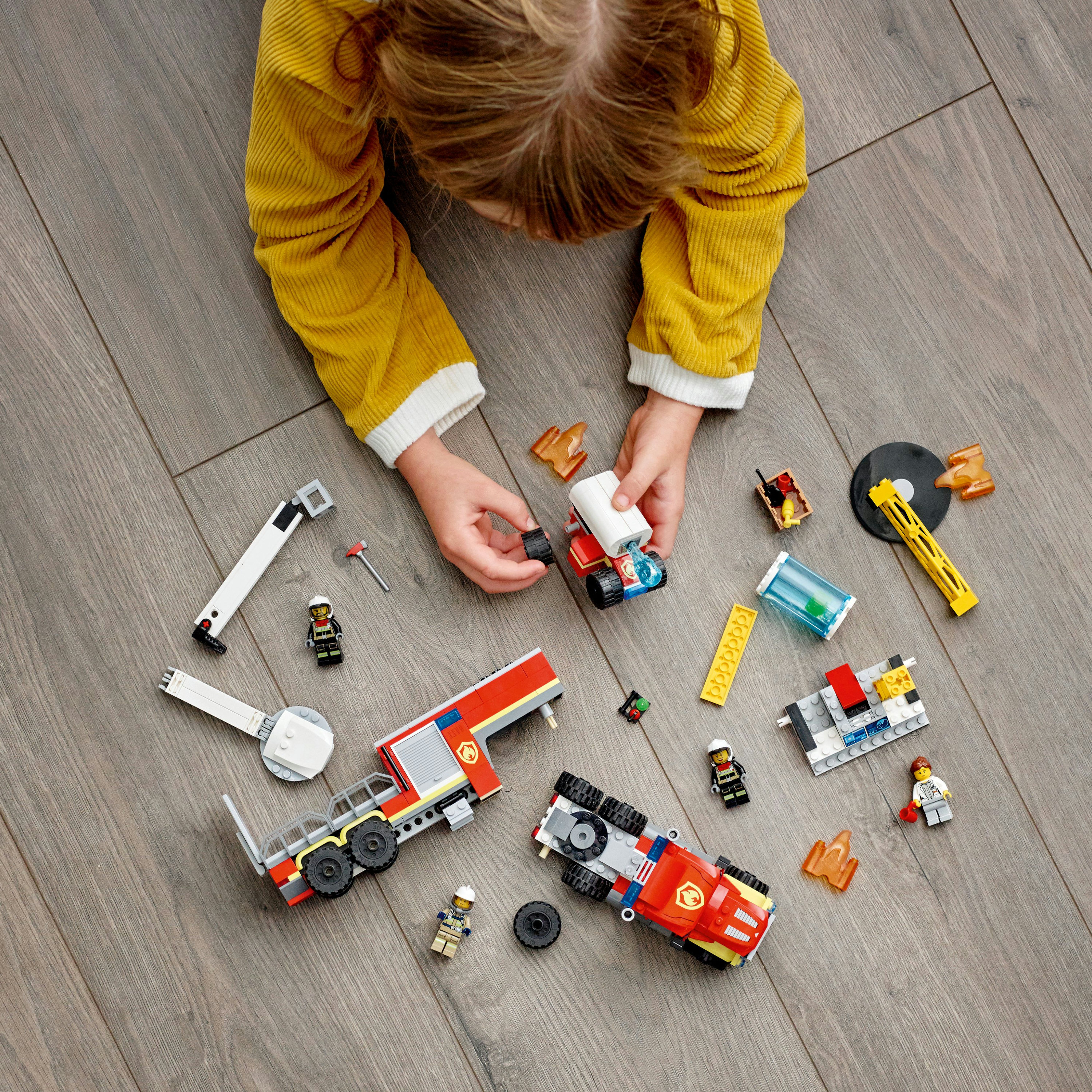 Un bambino sta costruendo un set di autopompe LEGO su un pavimento di legno con altri giocattoli.