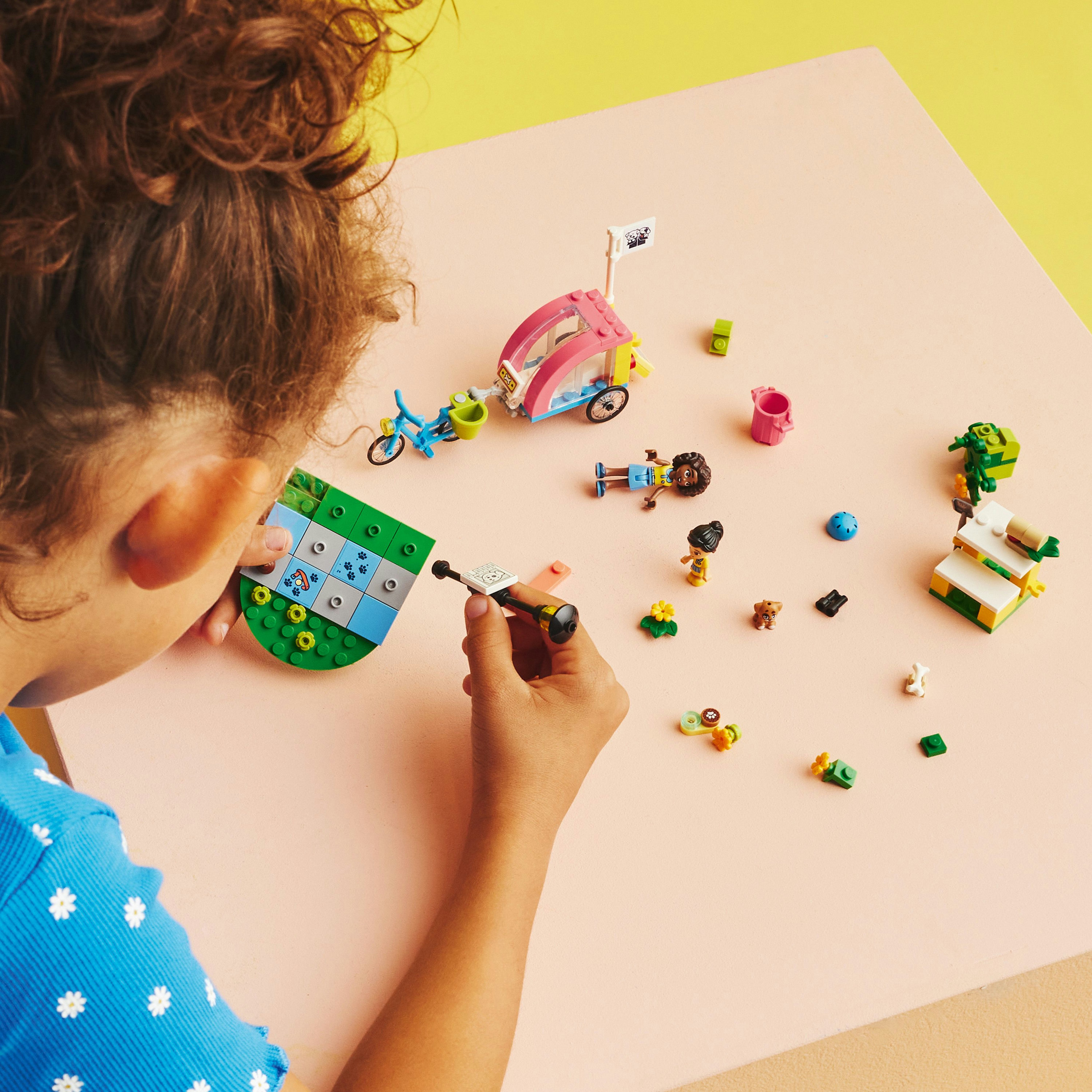Çocuğun Friends Lego setine bakışı. Çeşitli mini figürler ve aksesuarlarla pembe masa.