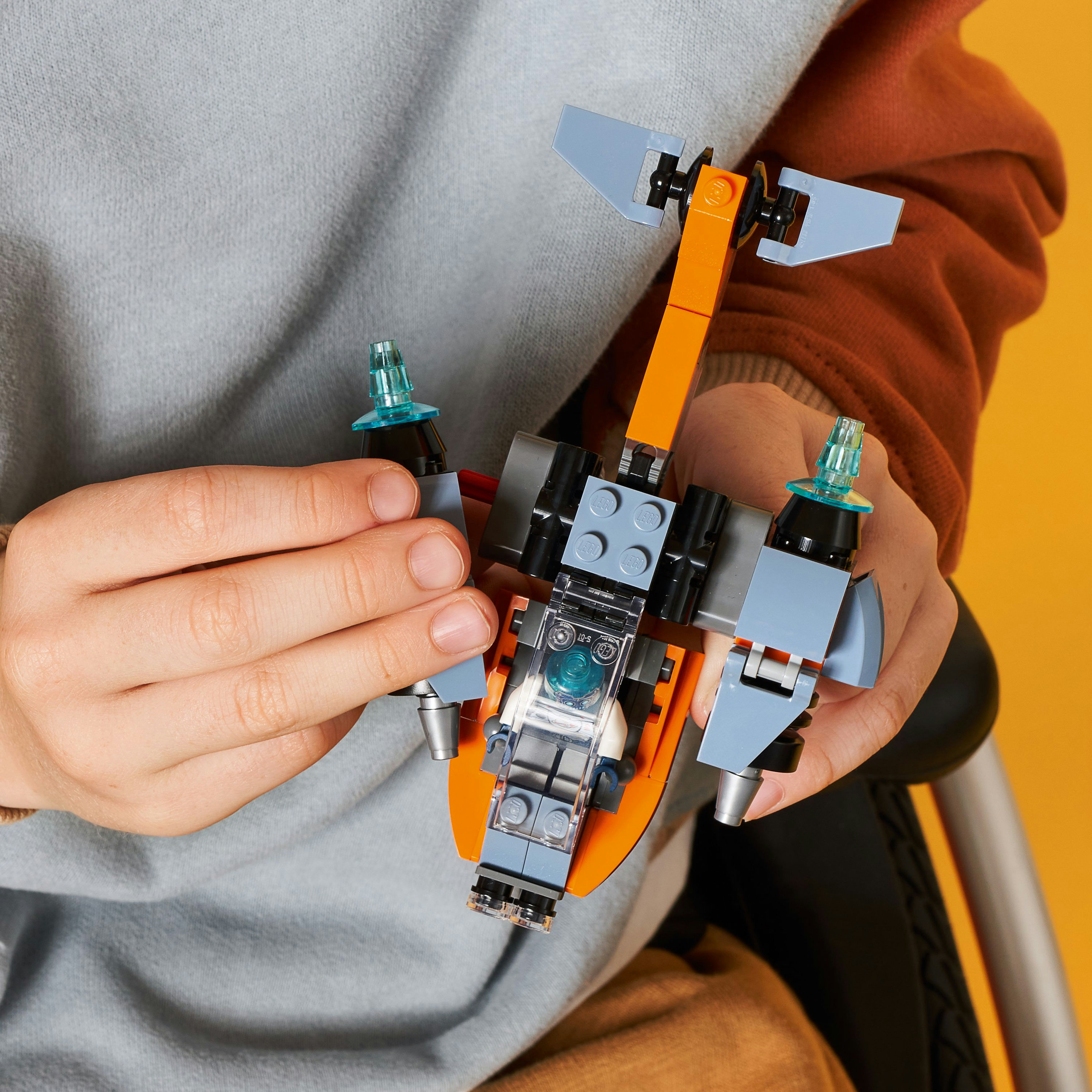 Ein Kind hält ein kleines Lego-Raumschiff. Das Schiff ist orange, grau und blau.