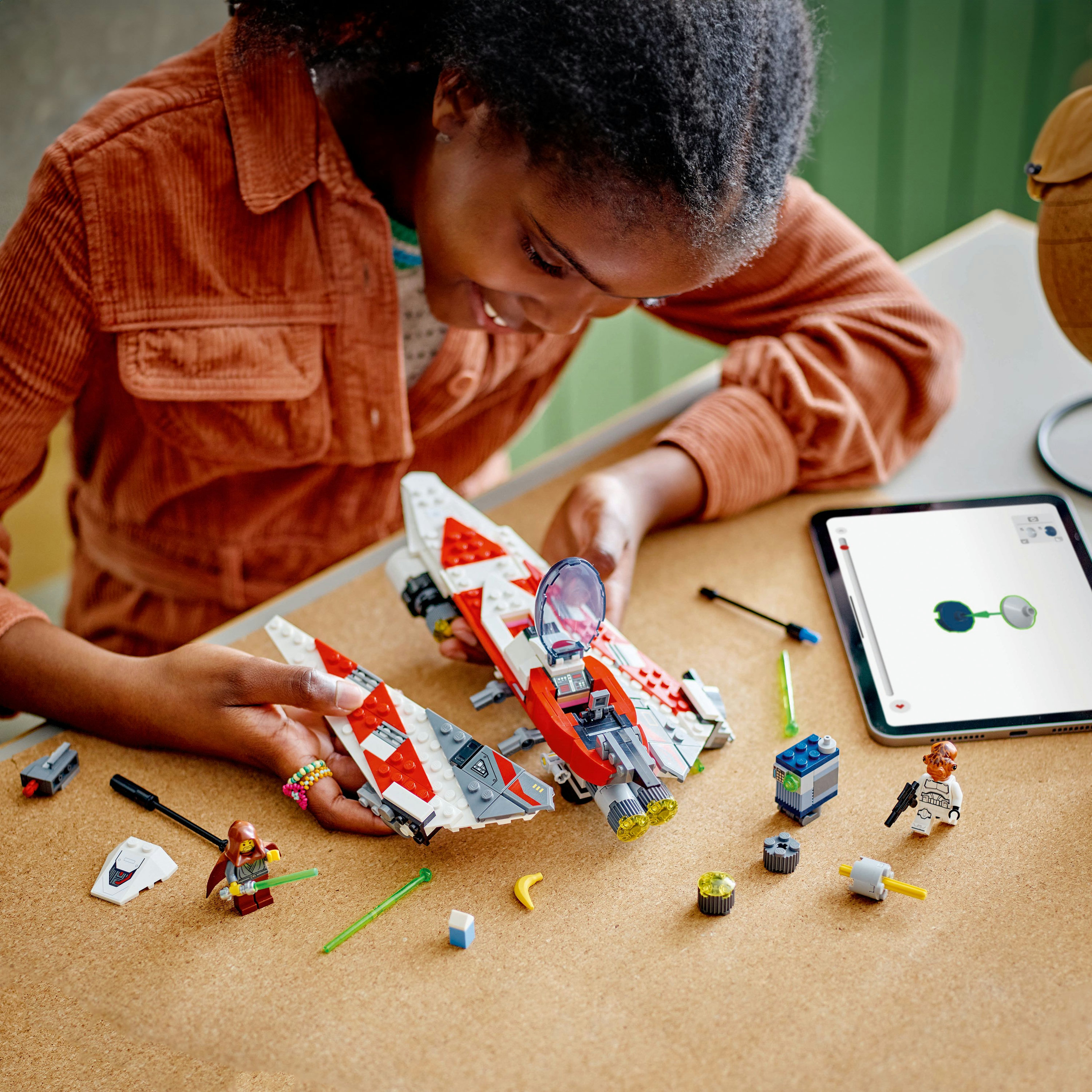 Dziecko buduje statek LEGO Star Wars. Czerwony, biały i szary statek. Części na drewnianym stole.