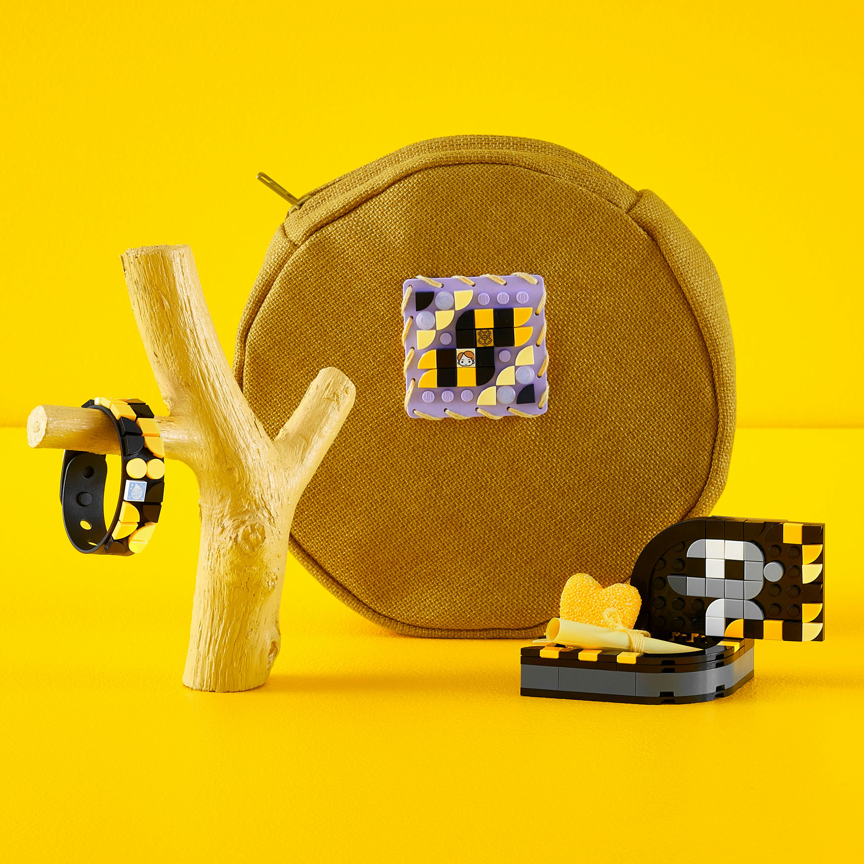 Sfondo giallo con accessori Lego: braccialetto, supporto, borsetta e una piccola scatola con un cuore giallo.