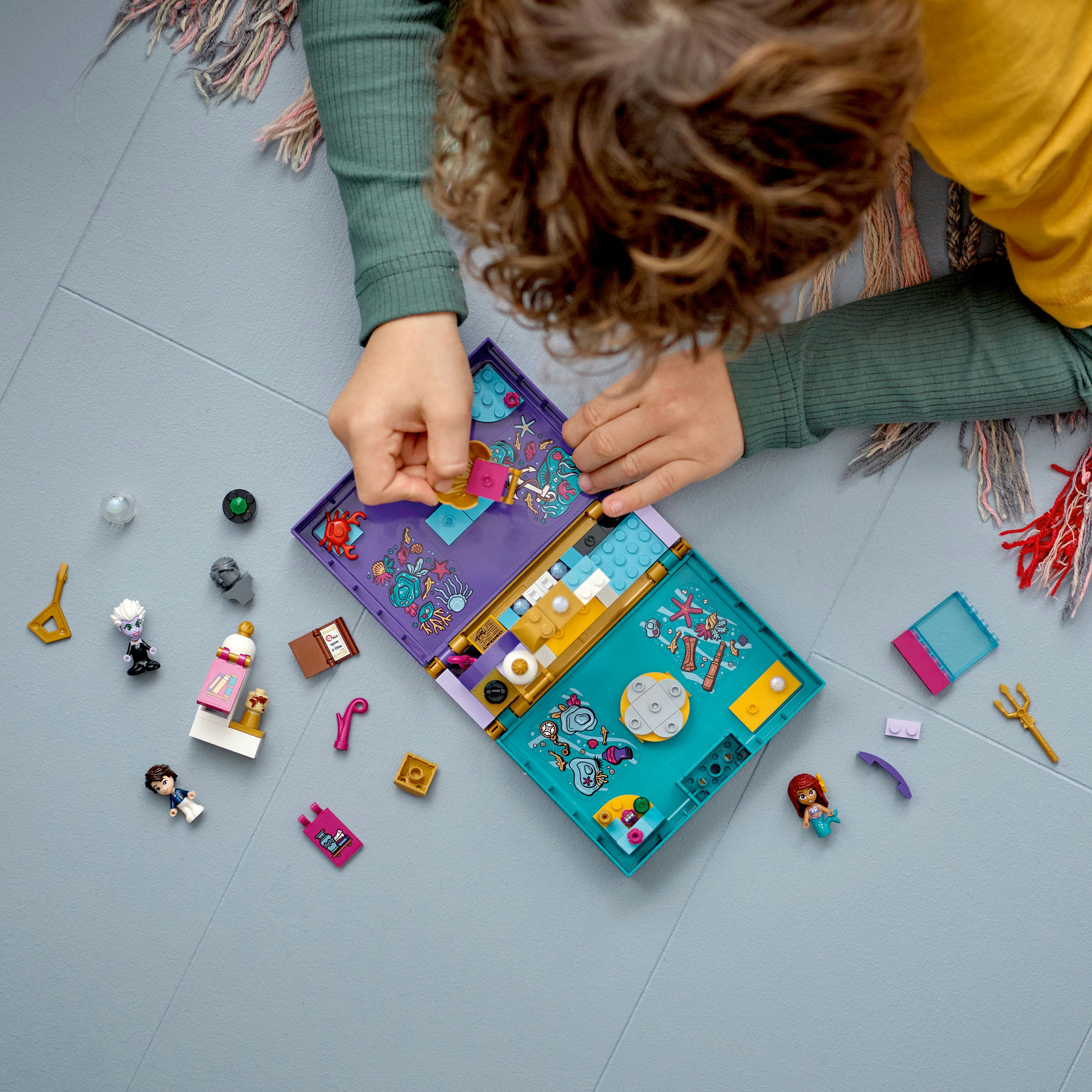 Niño jugando con set LEGO. Estructura abierta tipo libro rodeada de piezas LEGO y minifiguras.