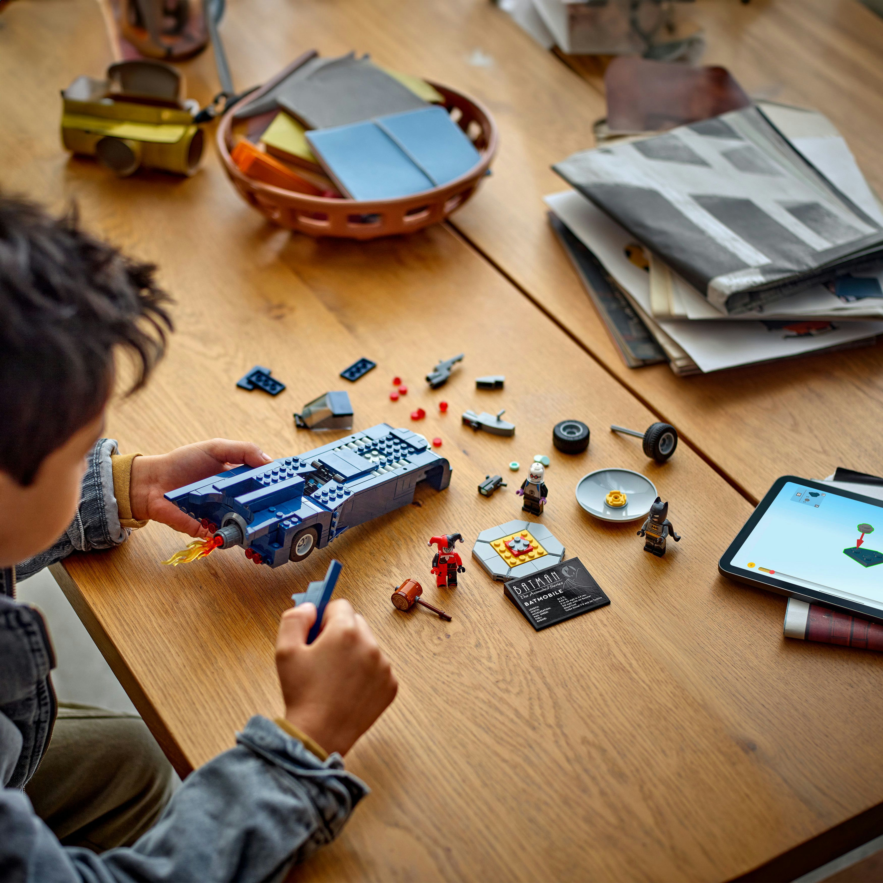 Dziecko budujące niebieski zestaw LEGO Batmobile, z figurkami i tabletem.