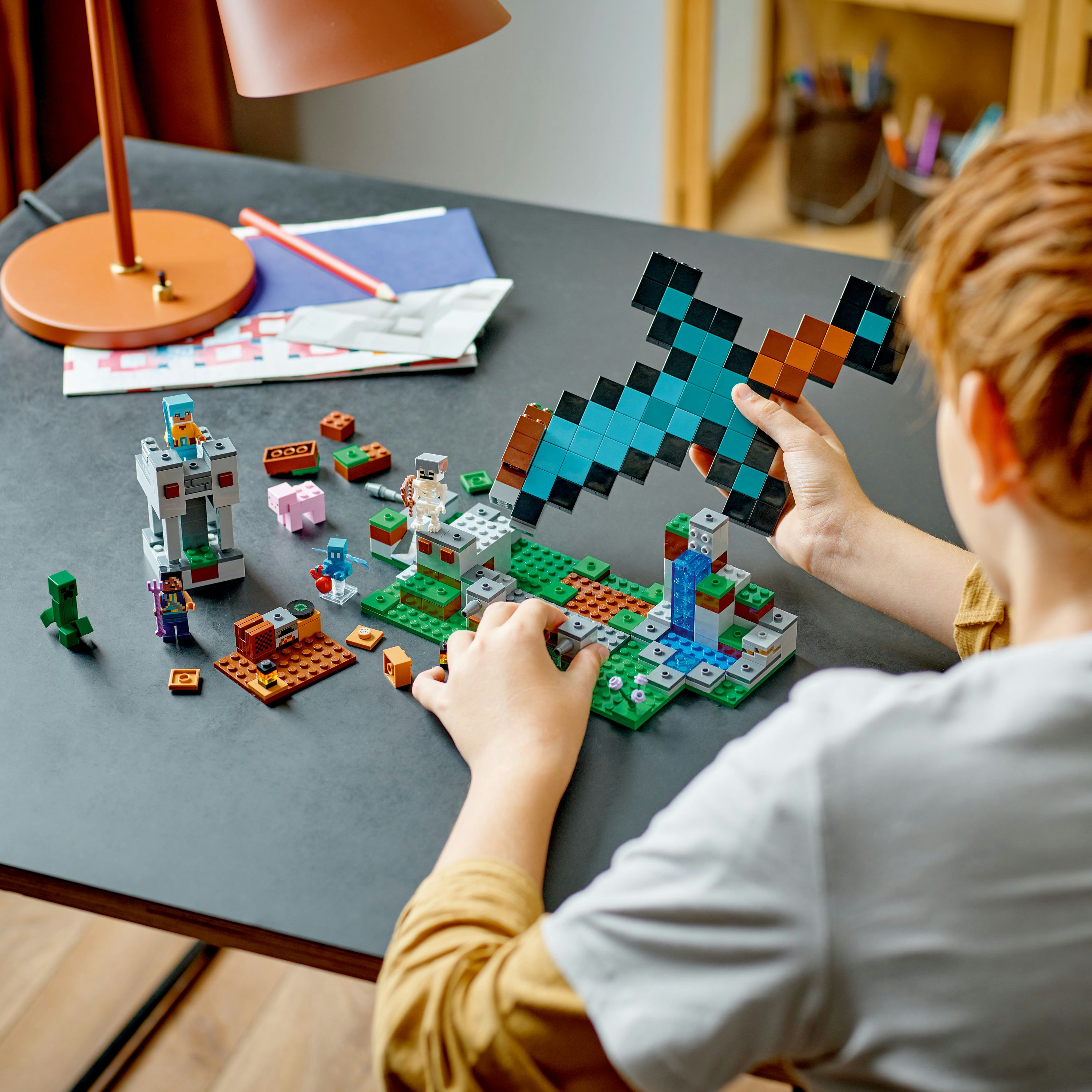Un enfant construisant un set LEGO Minecraft, avec une grande épée pixélisée, sur un bureau.