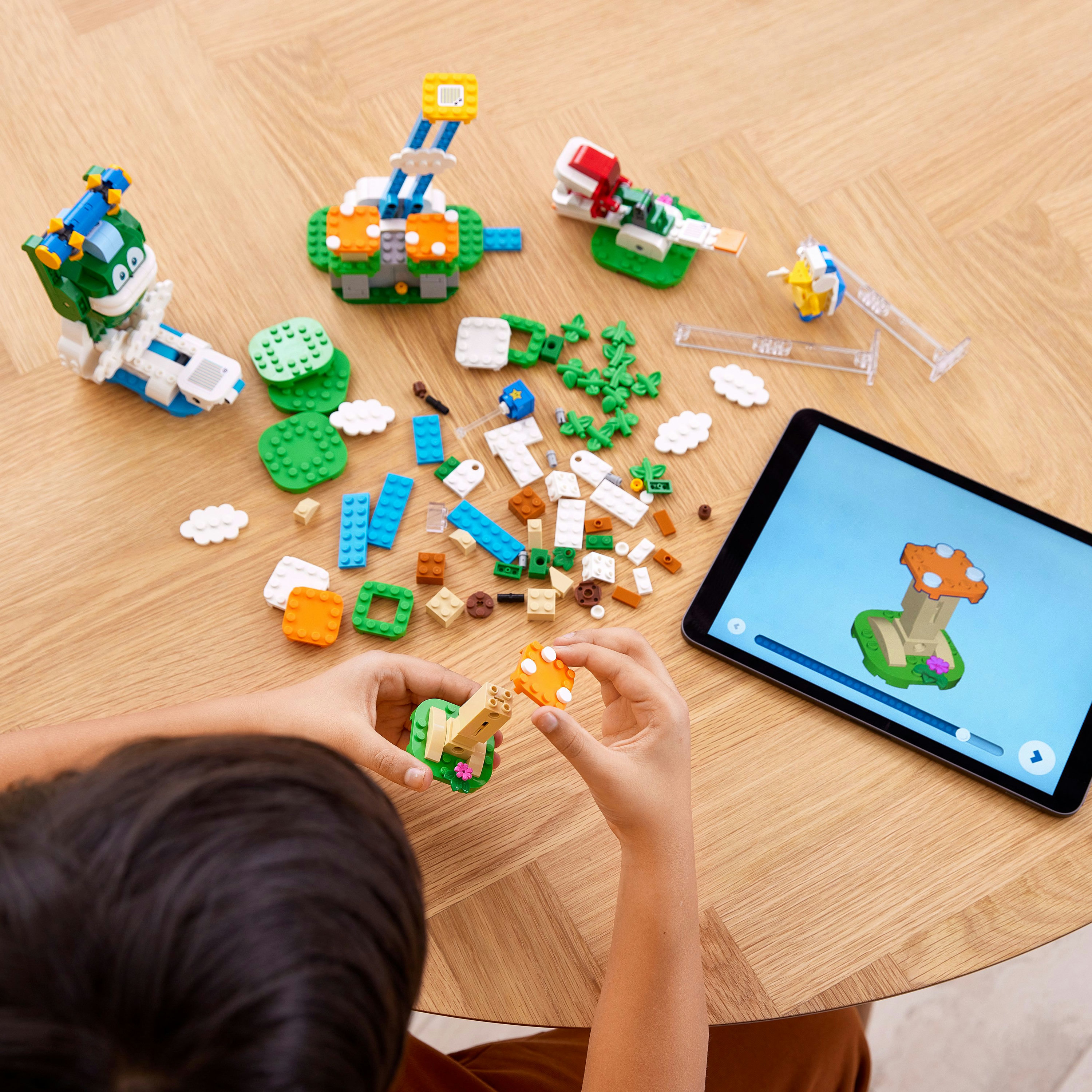 De handen van een kind dat Lego-stukjes op een tafel in elkaar zet met een tablet waarop een Lego-instructie staat.